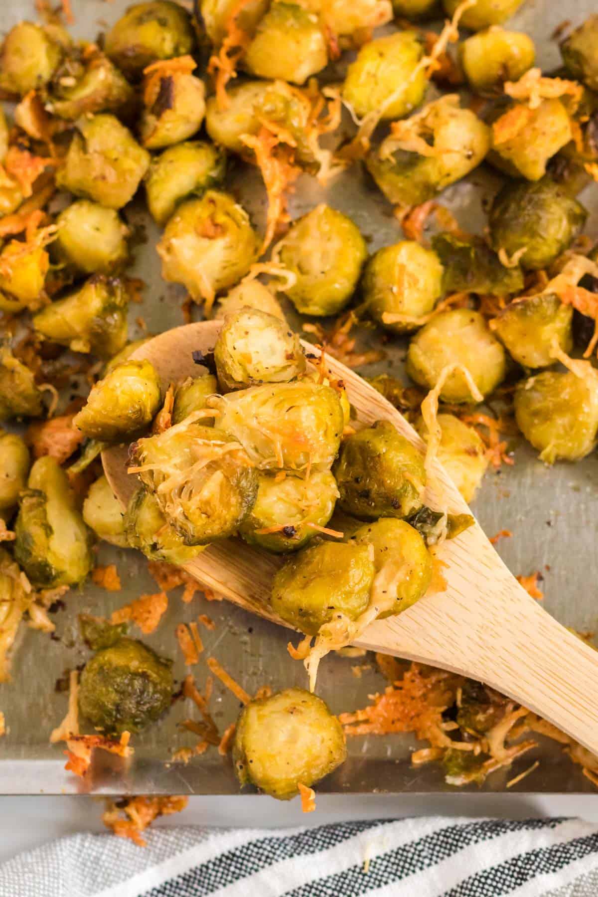 wooden spoon taking a serving of roasted brussels sprouts from the baking sheet