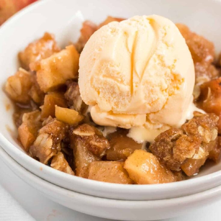 vegan apple crisp in a bowl topped with a scoop of ice cream