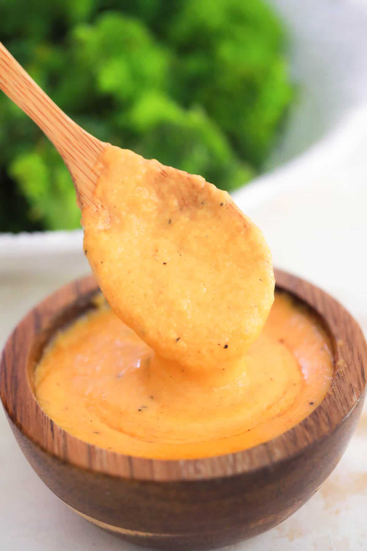 a wooden spoon taking cheese sauce from a bowl