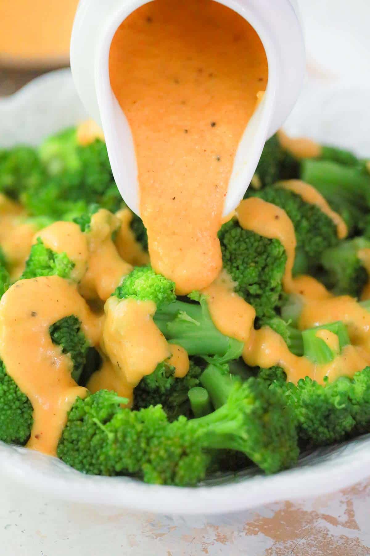 cheese sauce being poured over broccoli