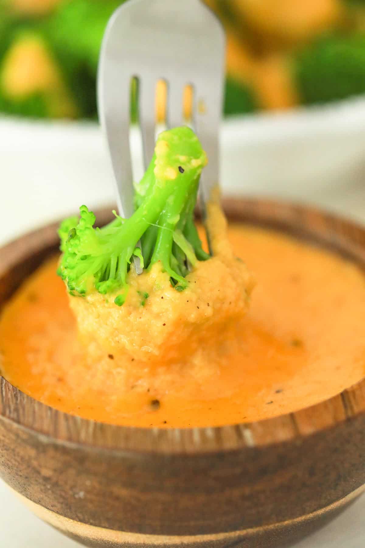 a fork dipping broccoli into a bowl of cheese sauce