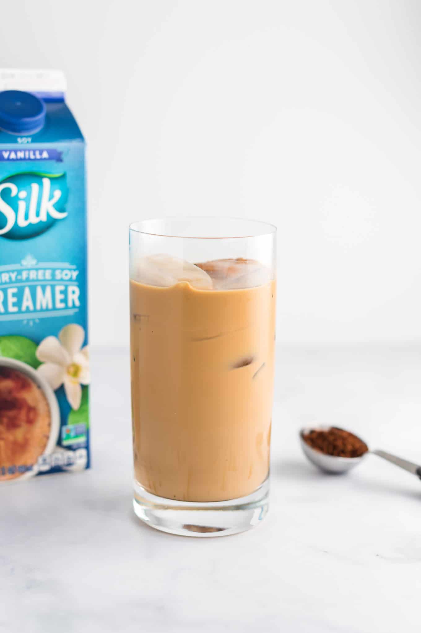 coffee in a glass with creamer and instant coffee grounds in the background