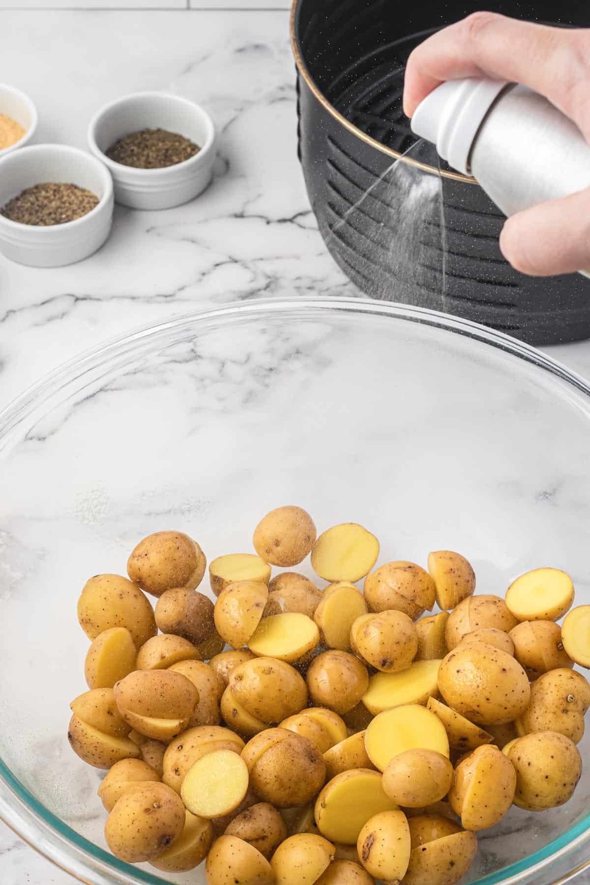 spraying a bowl of potatoes with olive oil spray