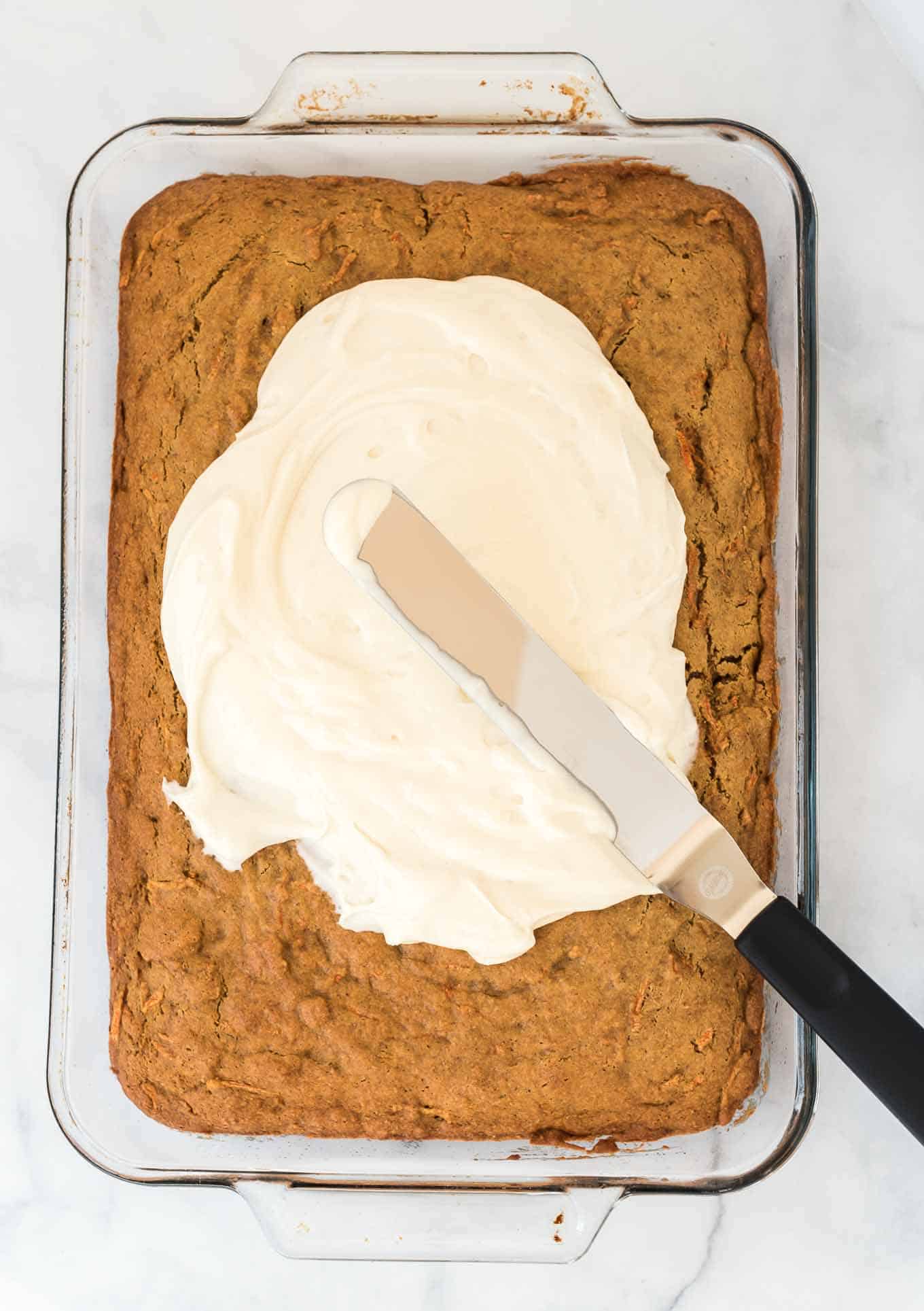 sheet pan carrot cake with frosting being spread on top
