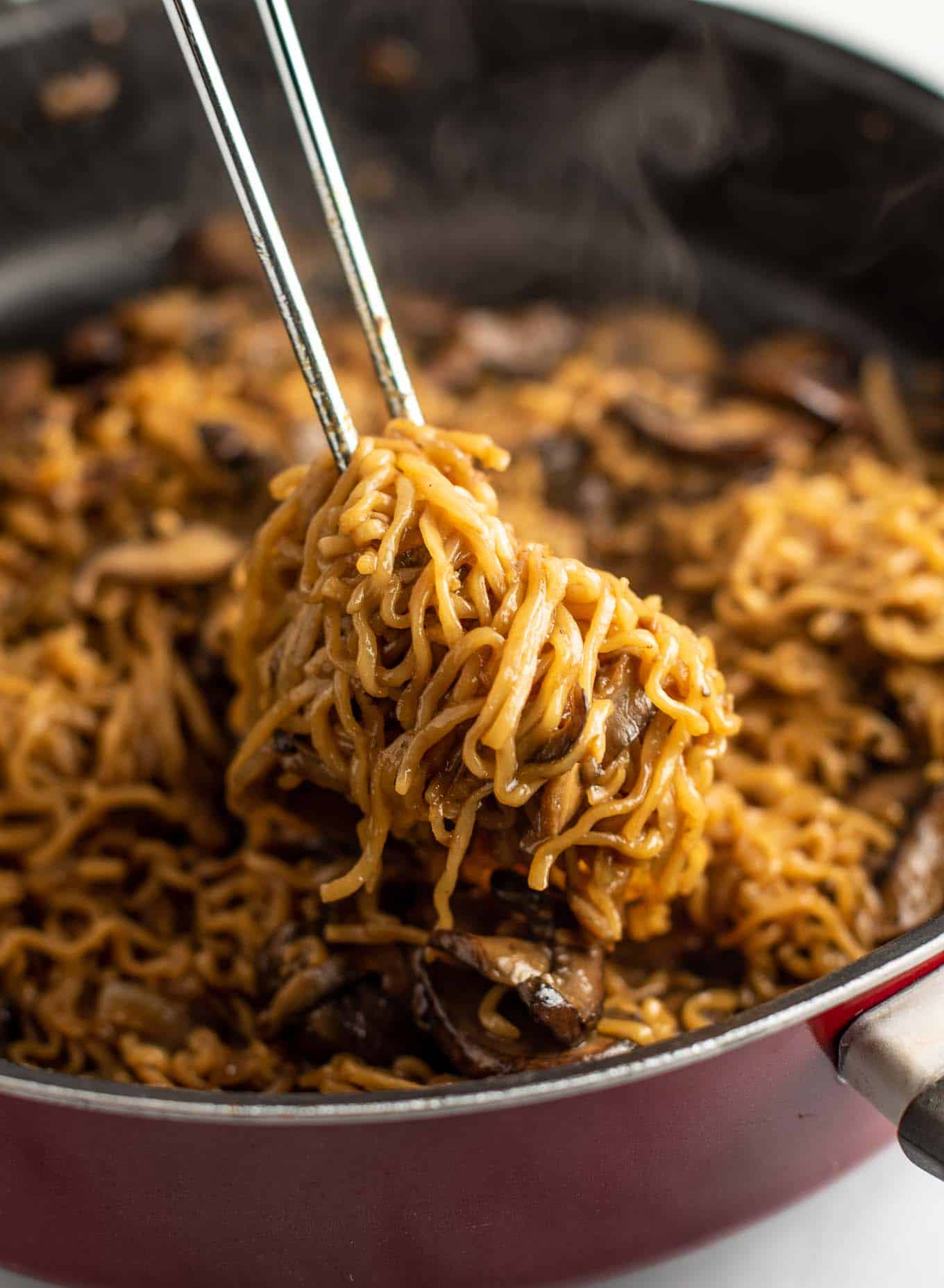 tongs pulling ramen noodles from a pan