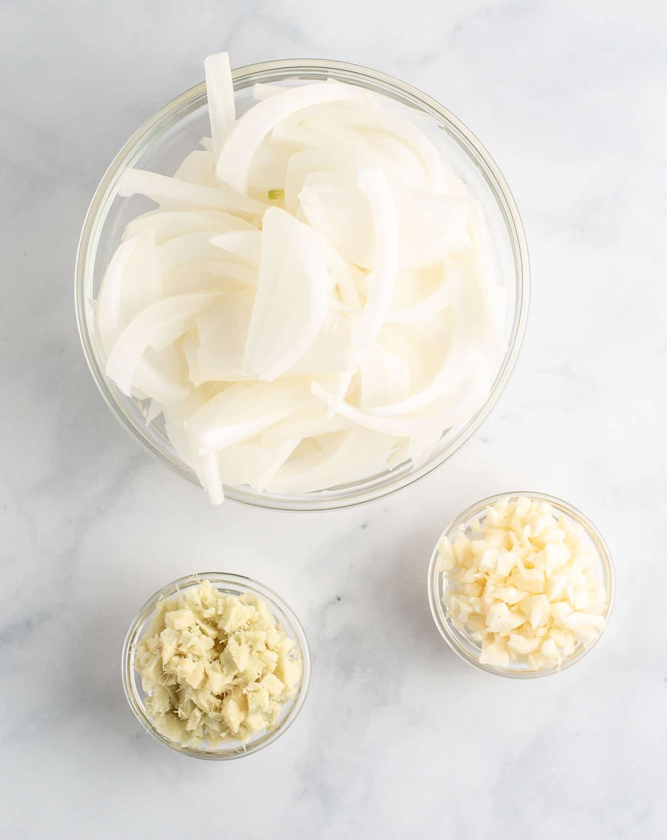 minced garlic, sliced onion, and minced ginger in bowls from an overhead view