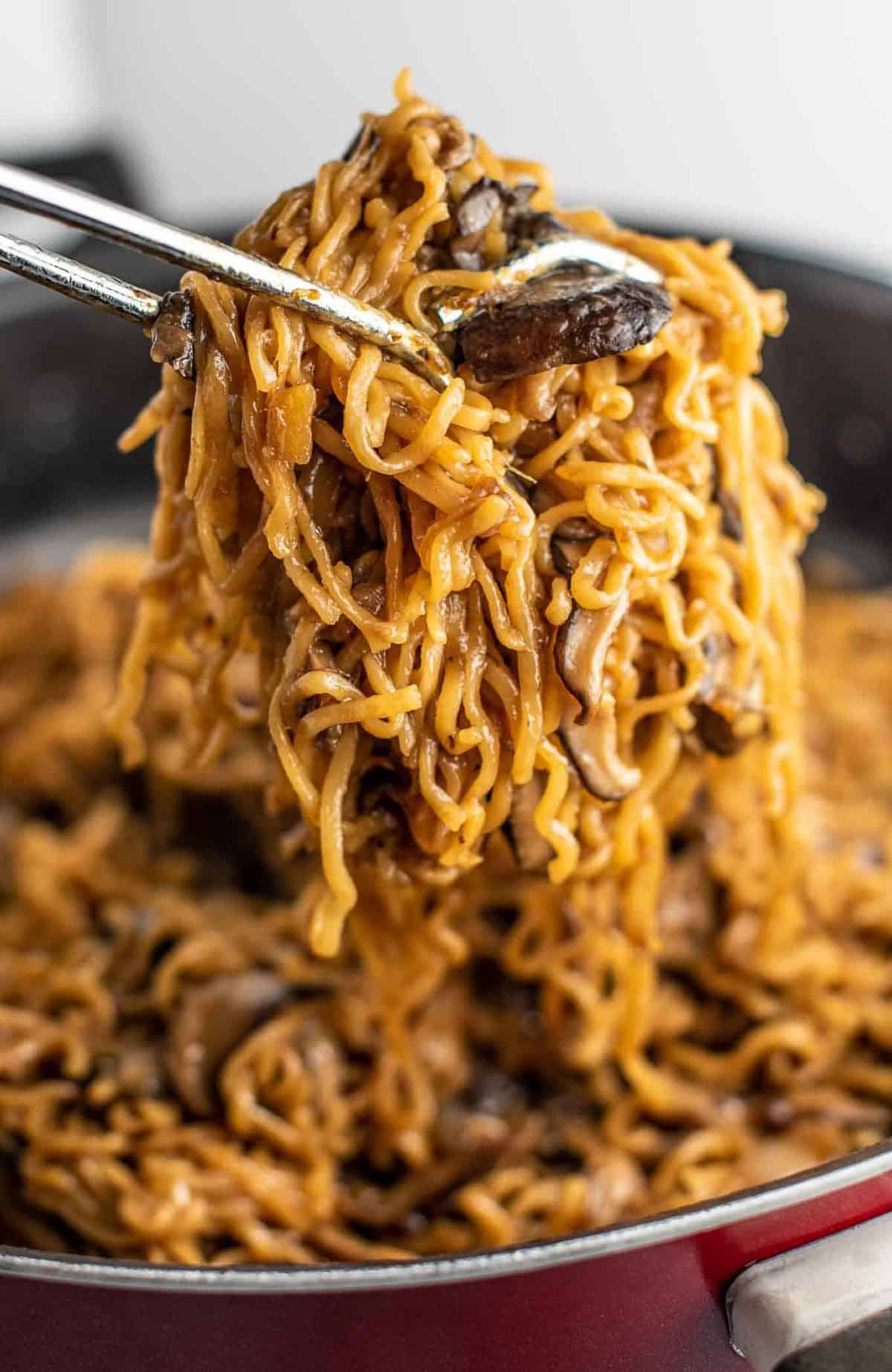 ramen noodles with mushrooms being pulled with tongs from a pan