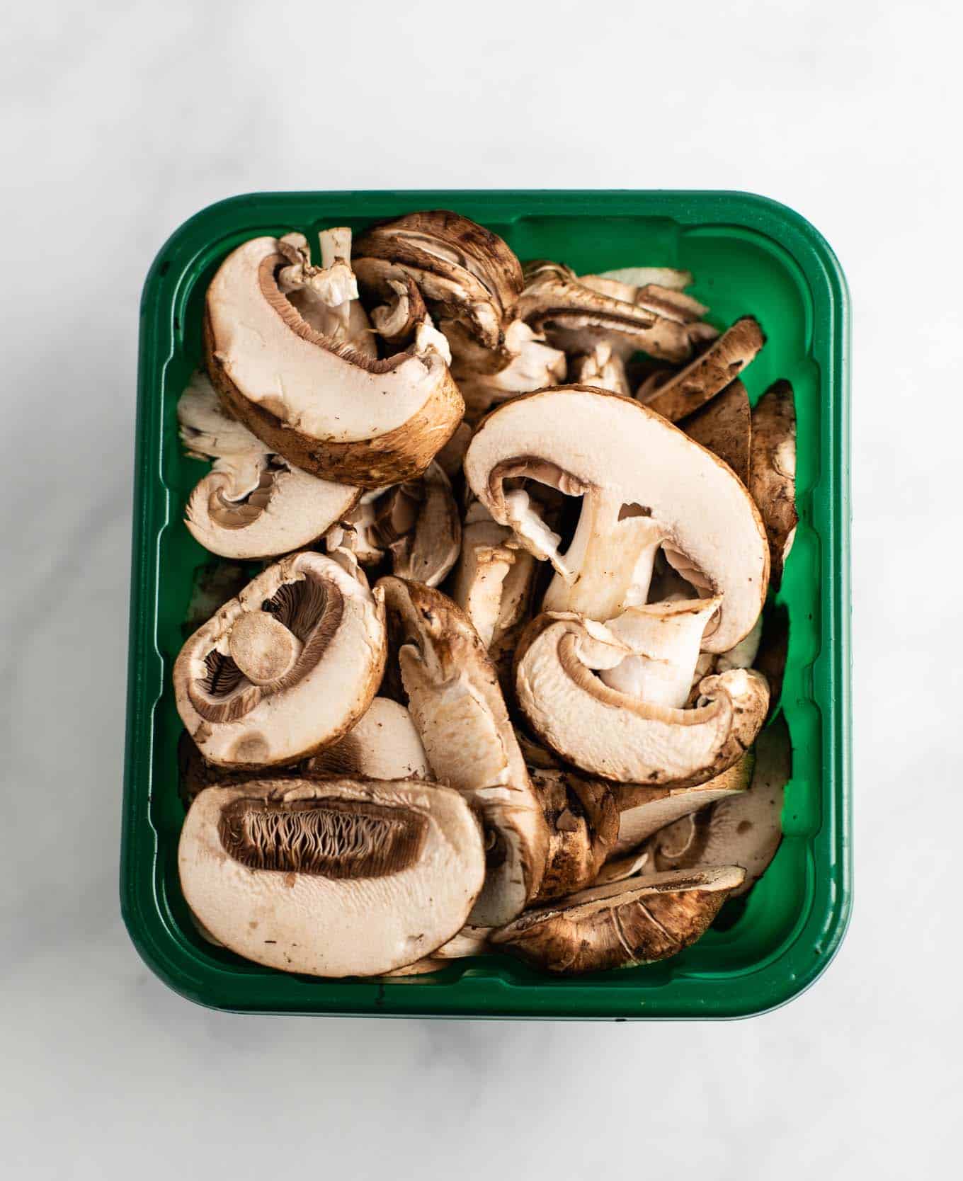 sliced portobello mushrooms in a produce container from an overhead view