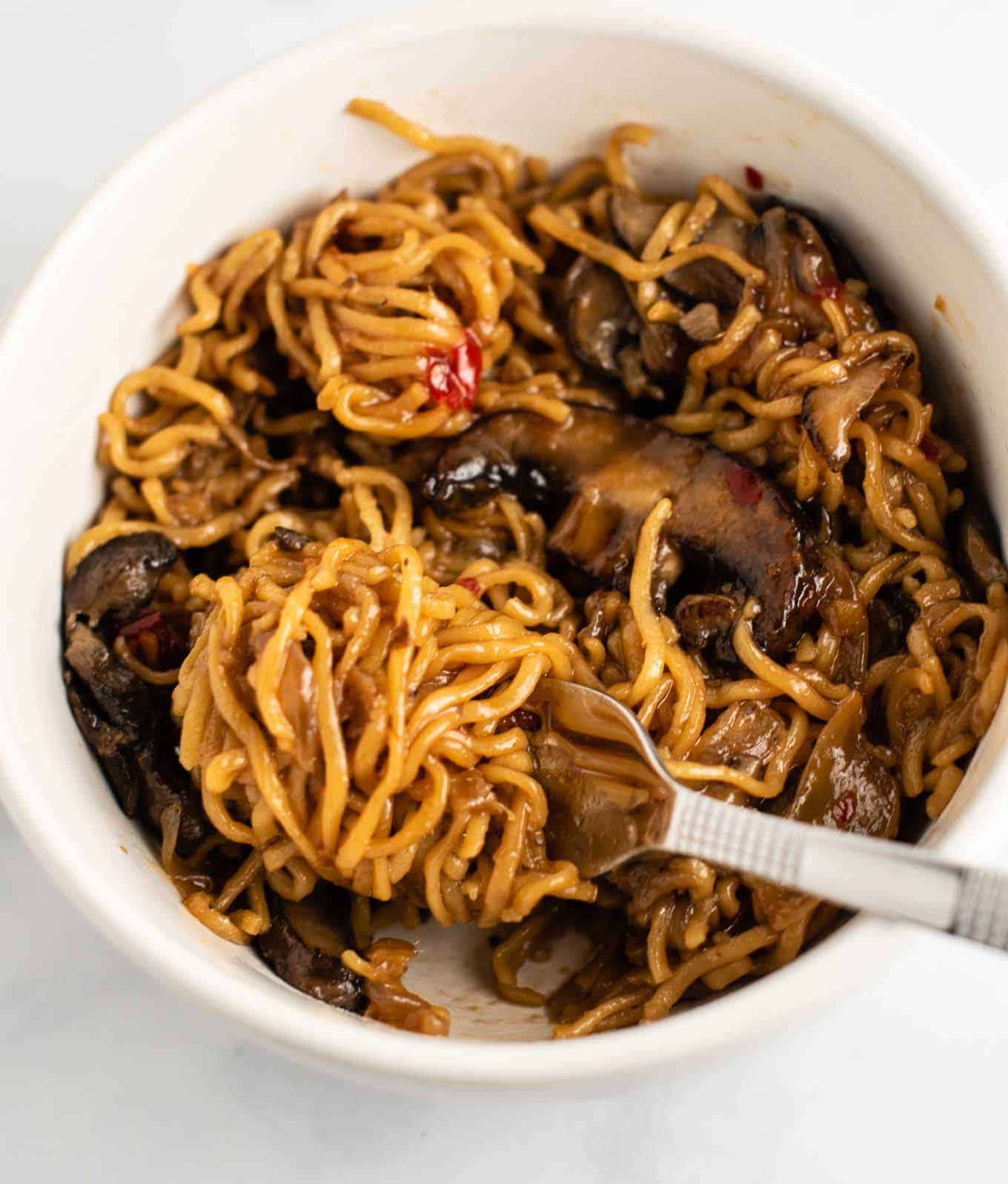 stir fry noodles with mushrooms and sweet chili sauce in a white bowl