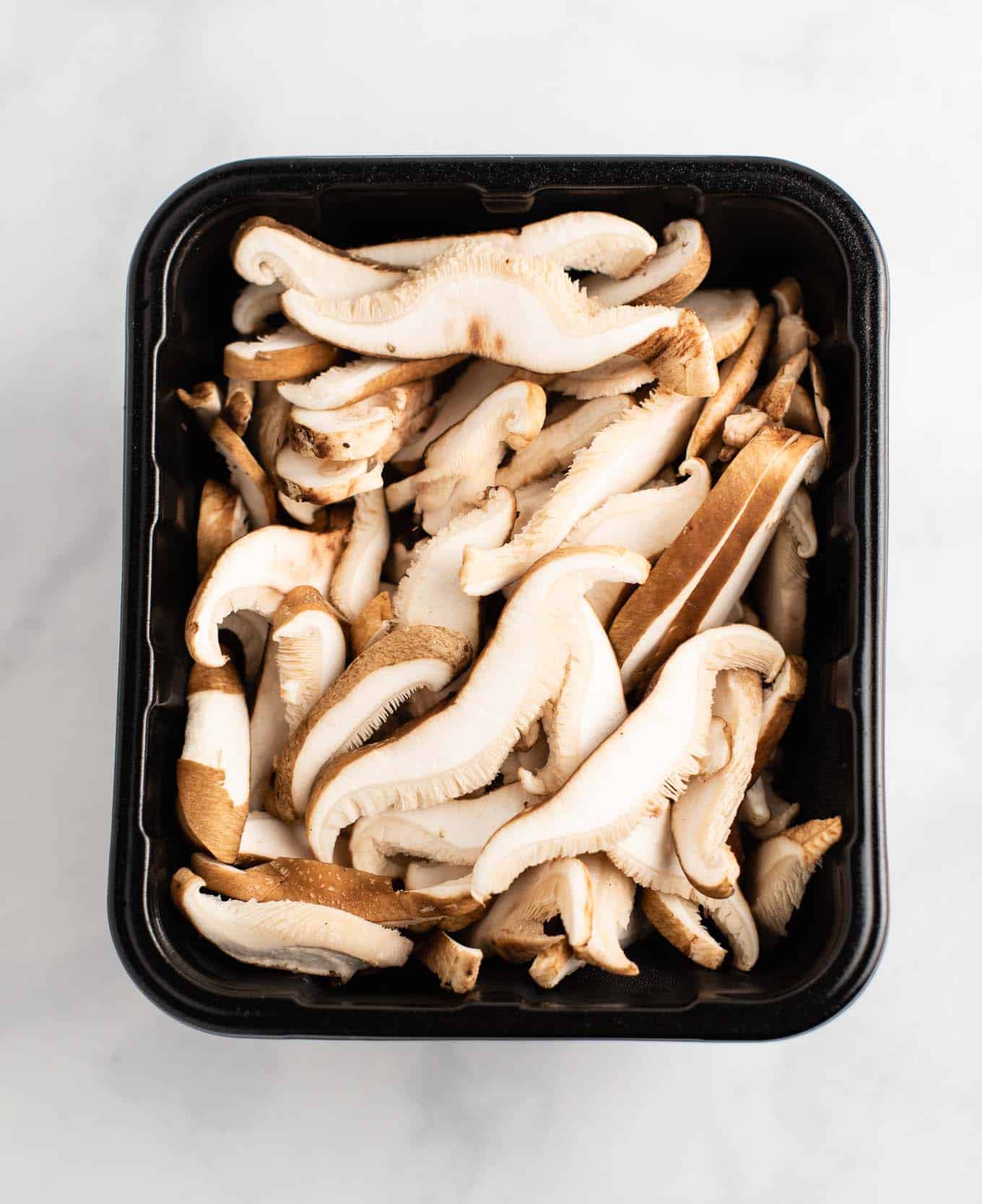 golden oak shitake sliced mushrooms in a produce container from an overhead view