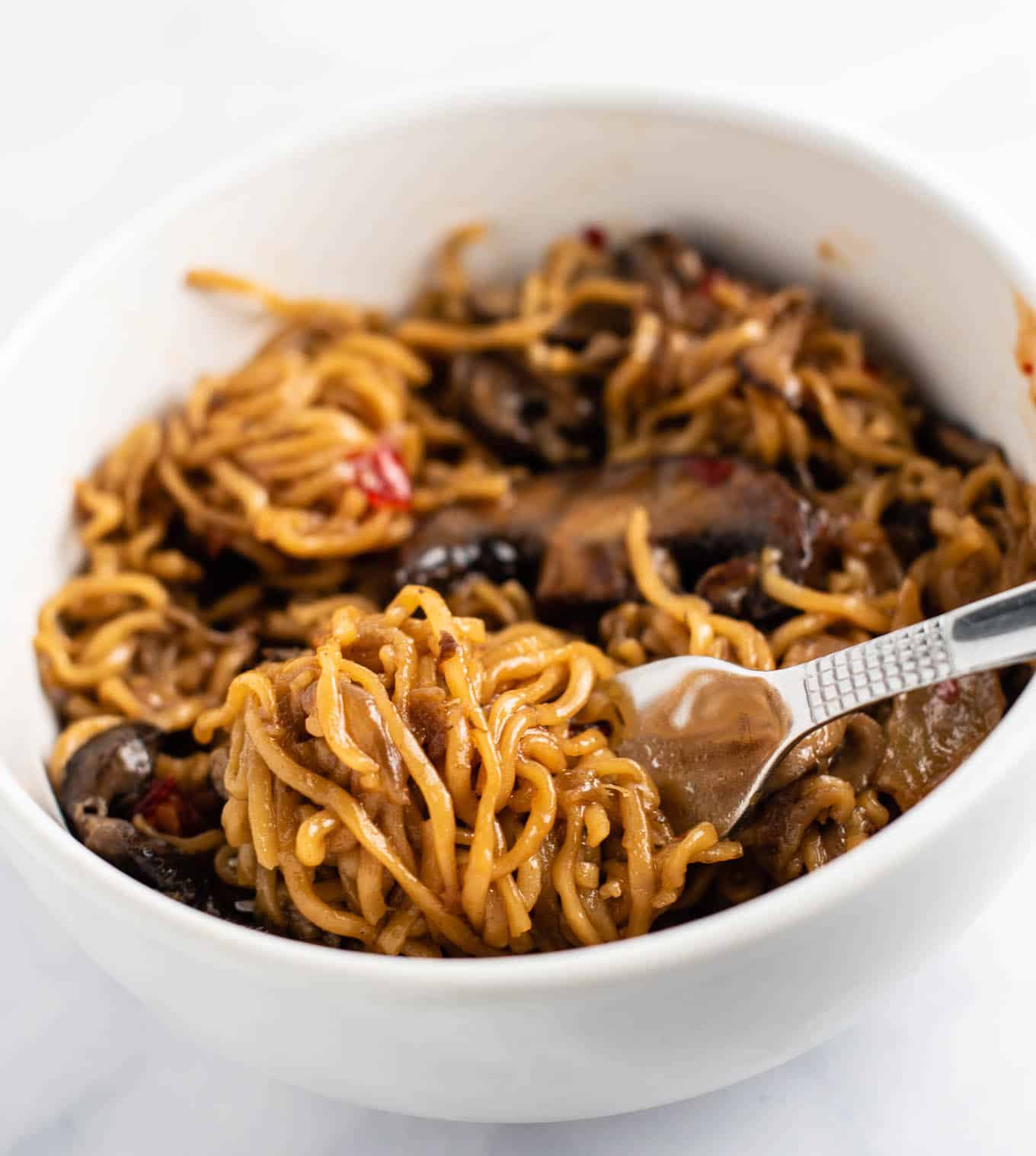 ramen noodles twirled on a fork resting on stir fry noodles in a white bowl