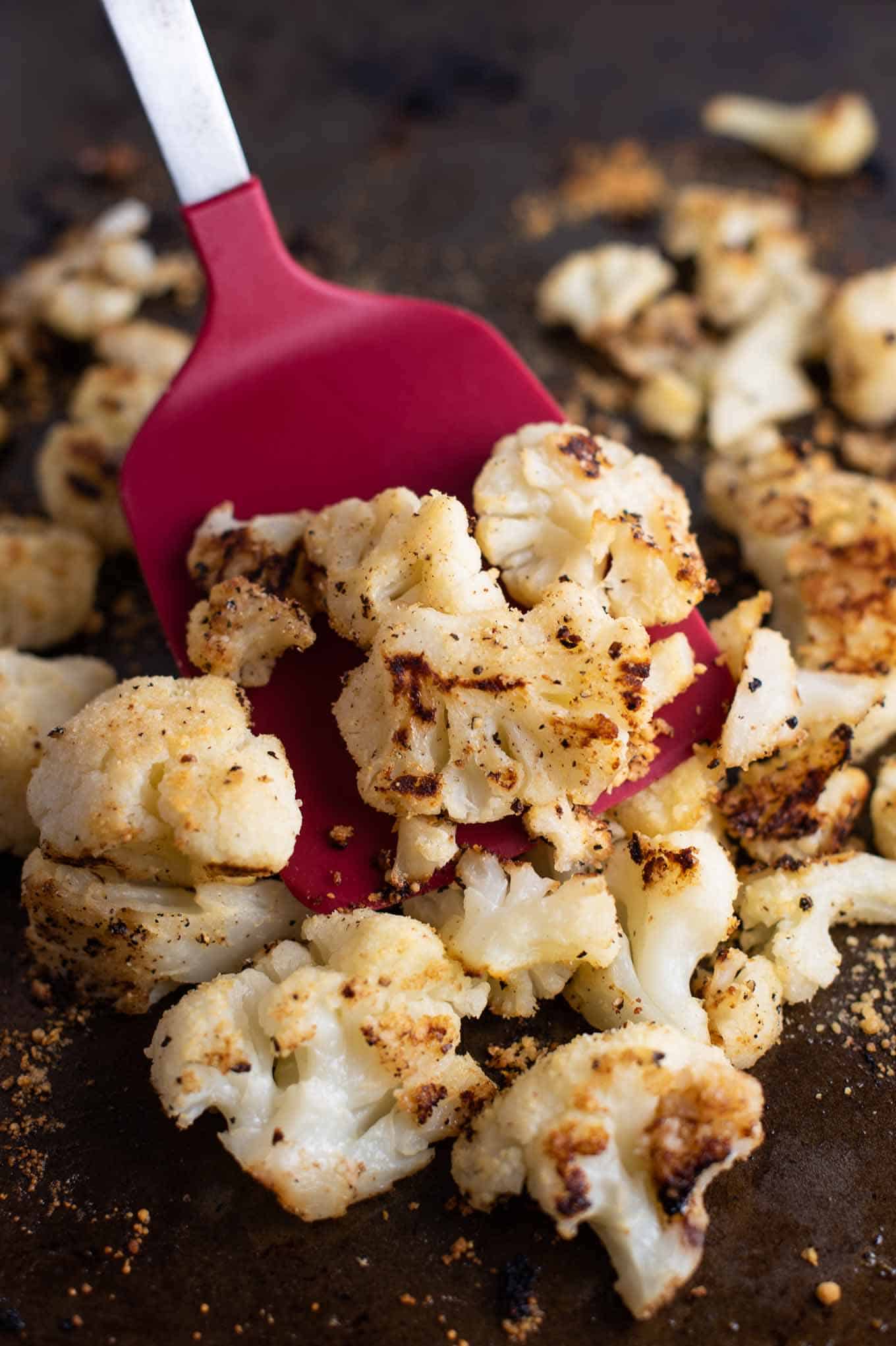 a red spatula picking up a scoop of roasted cauliflower