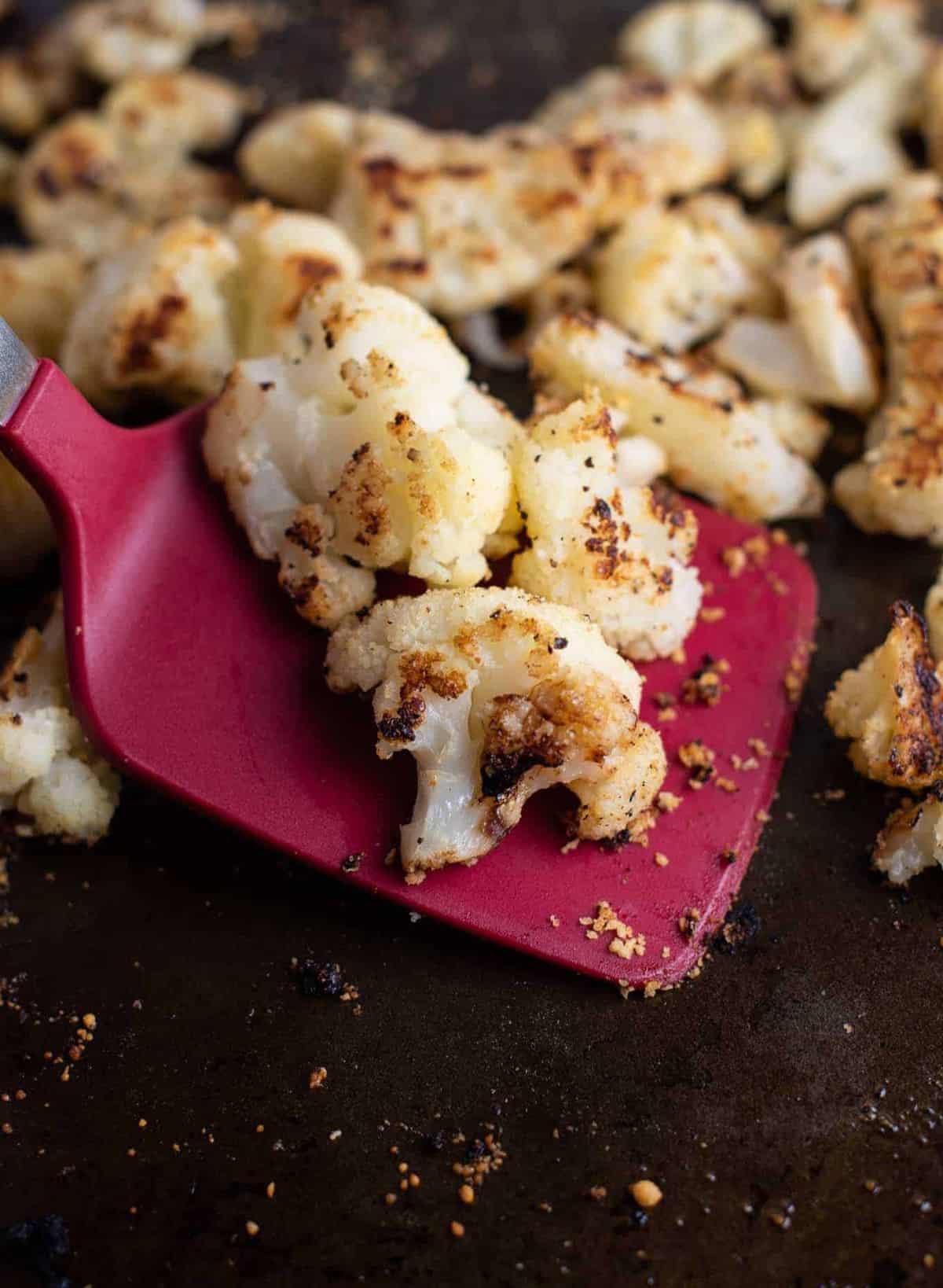 roasted frozen cauliflower on a baking sheet with a red spatula