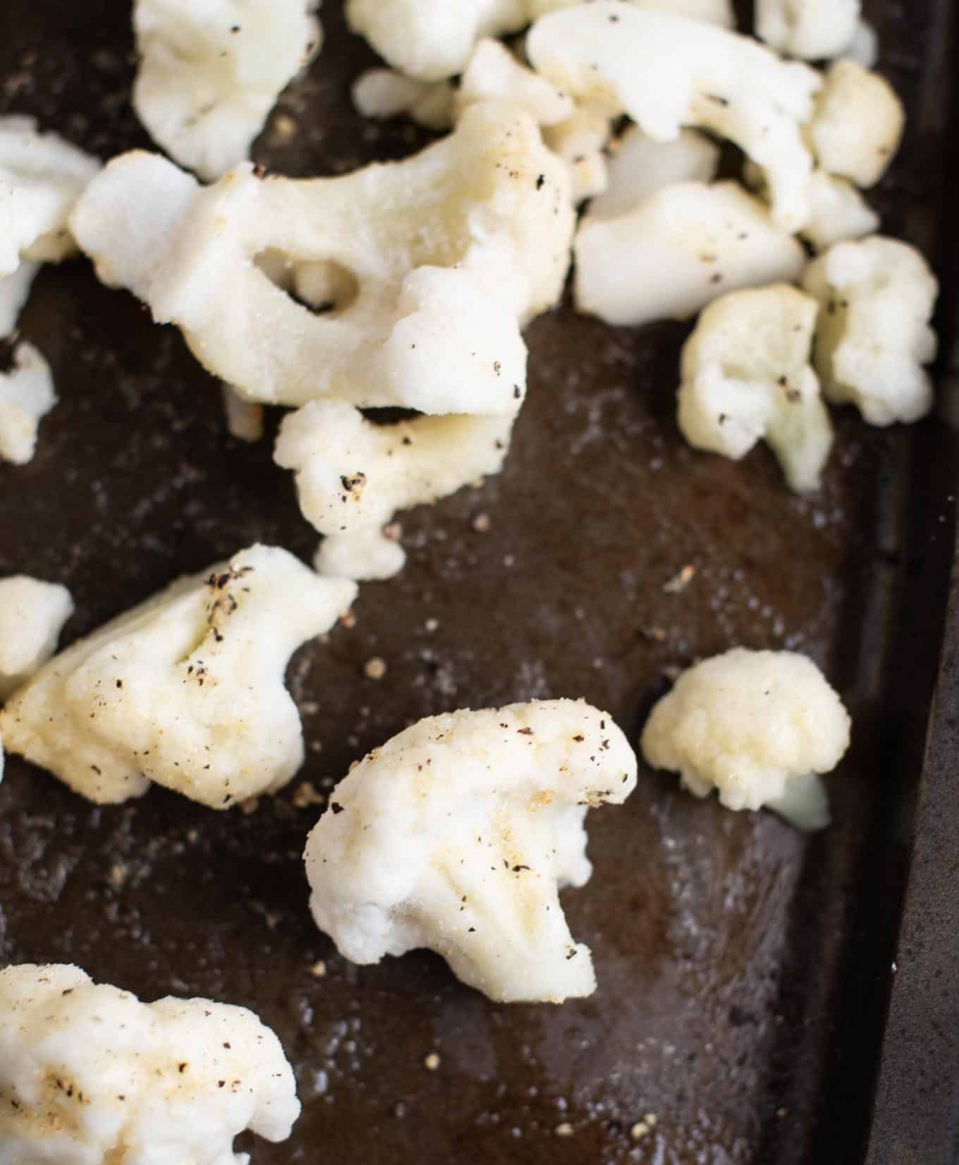 frozen cauliflower on a baking sheet with spices sprinkled on it before cooking