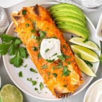 veggie enchiladas on a plate topped with sour cream and garnished with lime and avocado