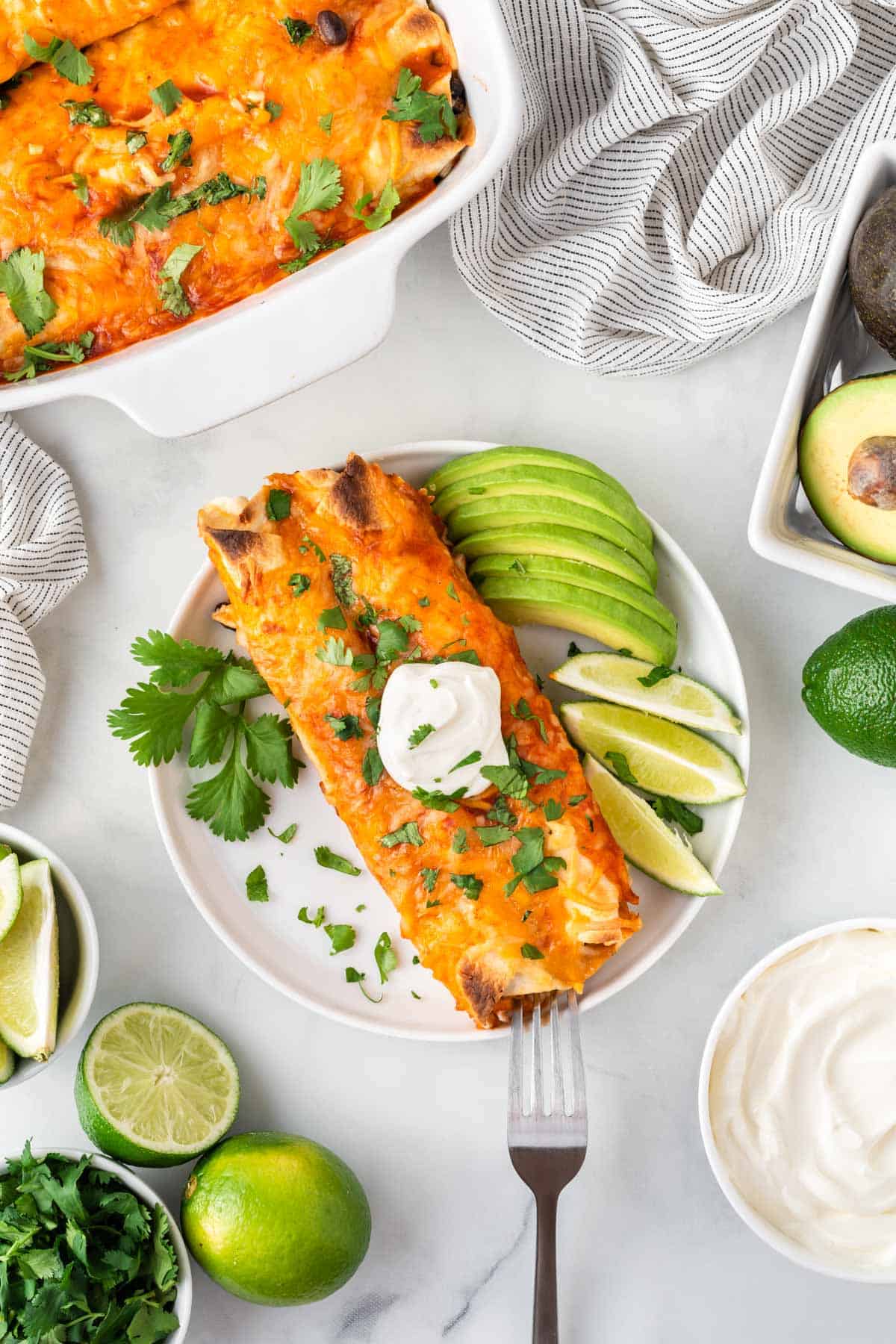 veggie enchiladas on a plate topped with sour cream and garnished with lime and avocado