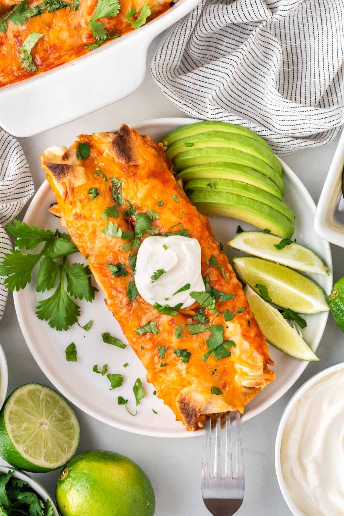 veggie enchiladas on a plate topped with sour cream and garnished with lime and avocado