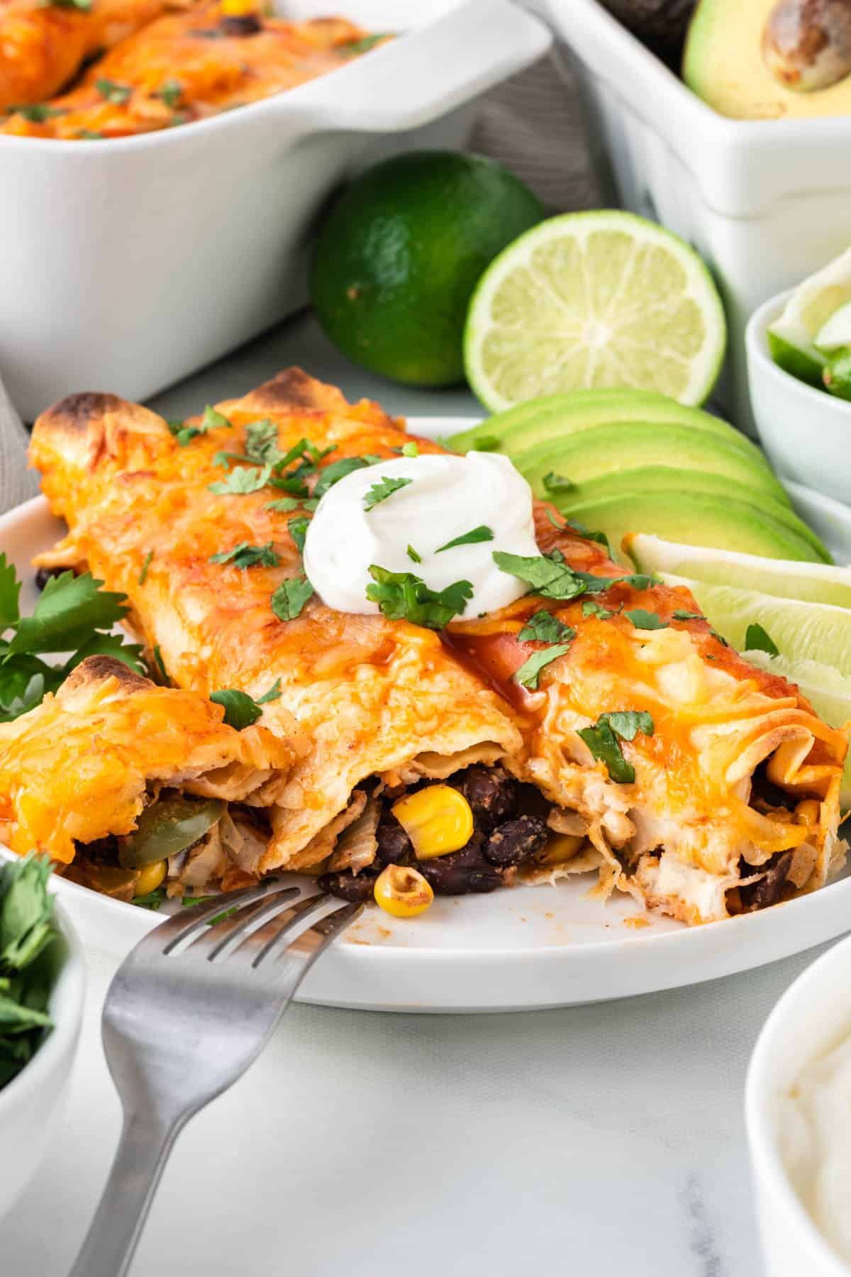 veggie enchiladas on a plate topped with sour cream and garnished with lime and avocado