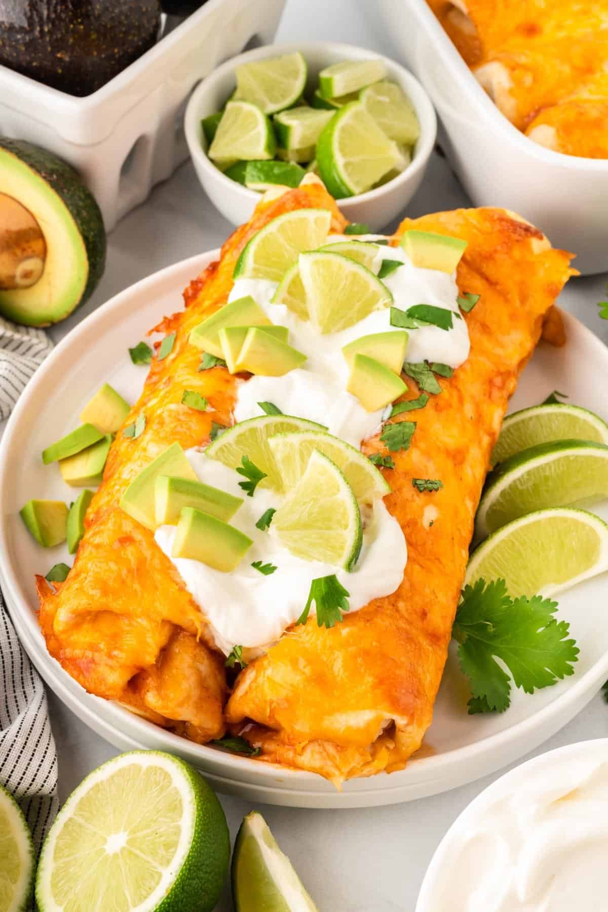two enchiladas on a plate topped with sour cream, avocado, and lime
