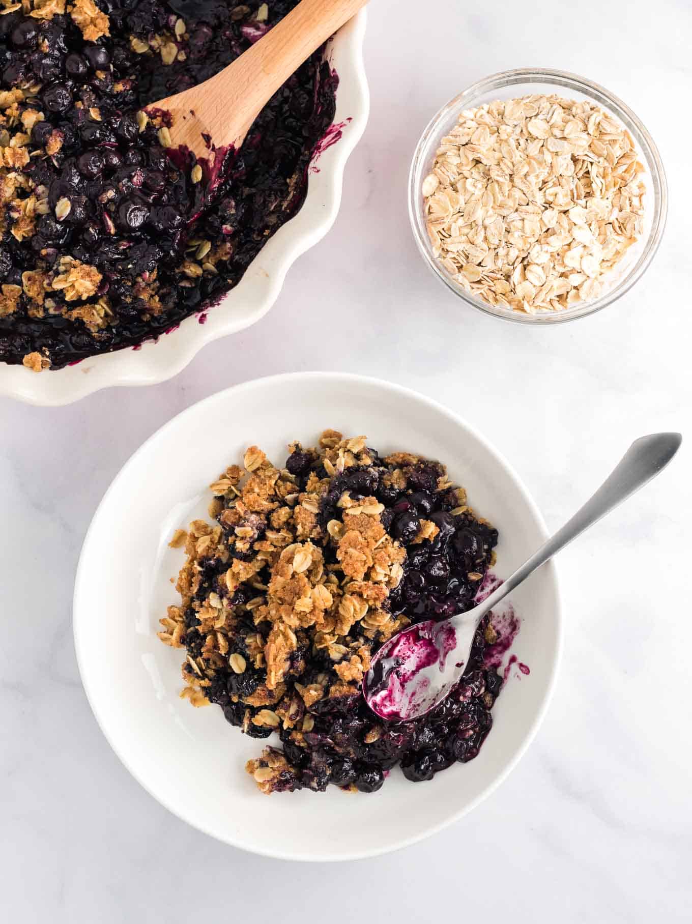blueberry crisp in a white bowl with a silver spoon from an overhead view