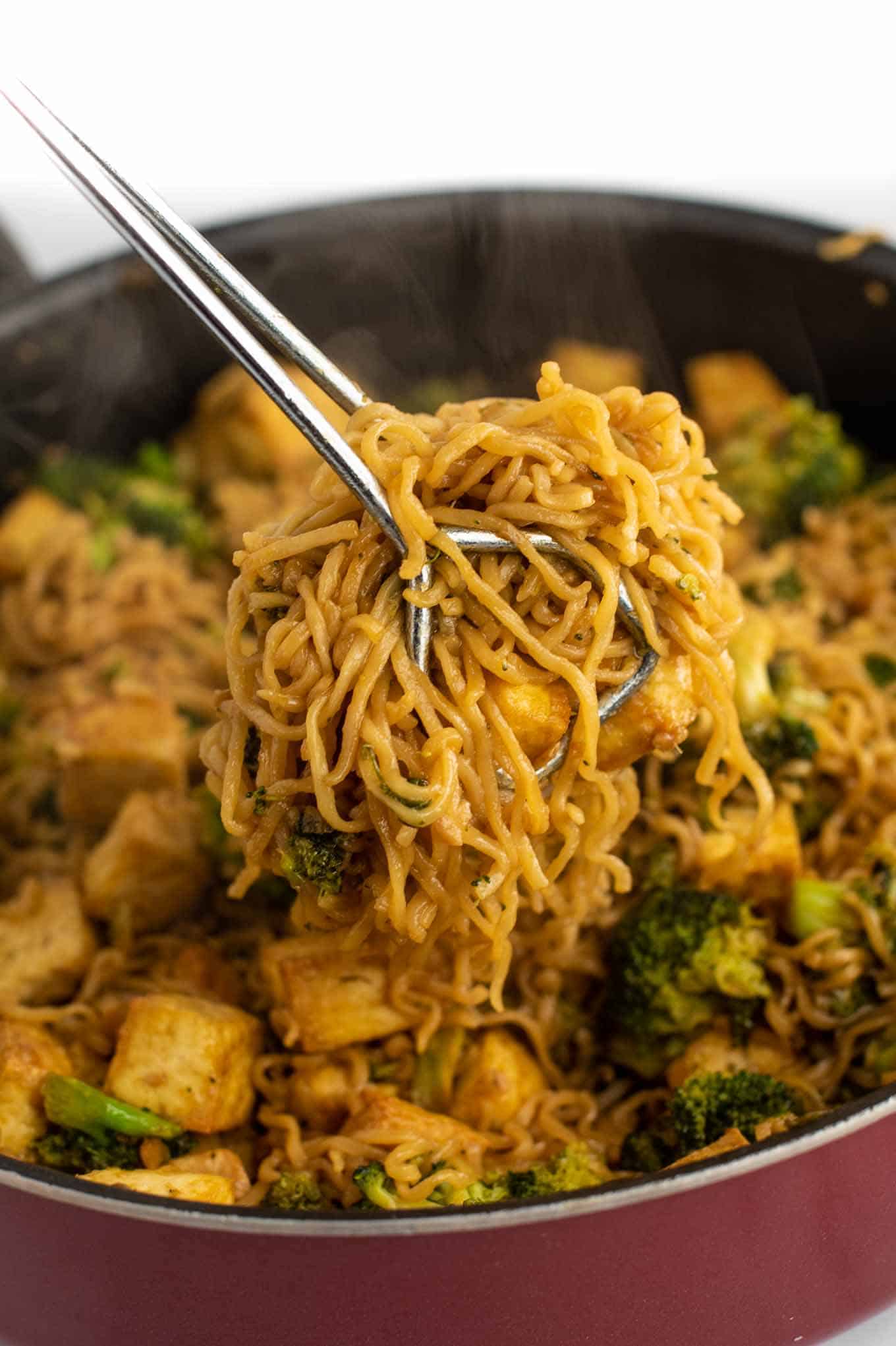 tongs grabbing a serving of ramen noodle stir fry