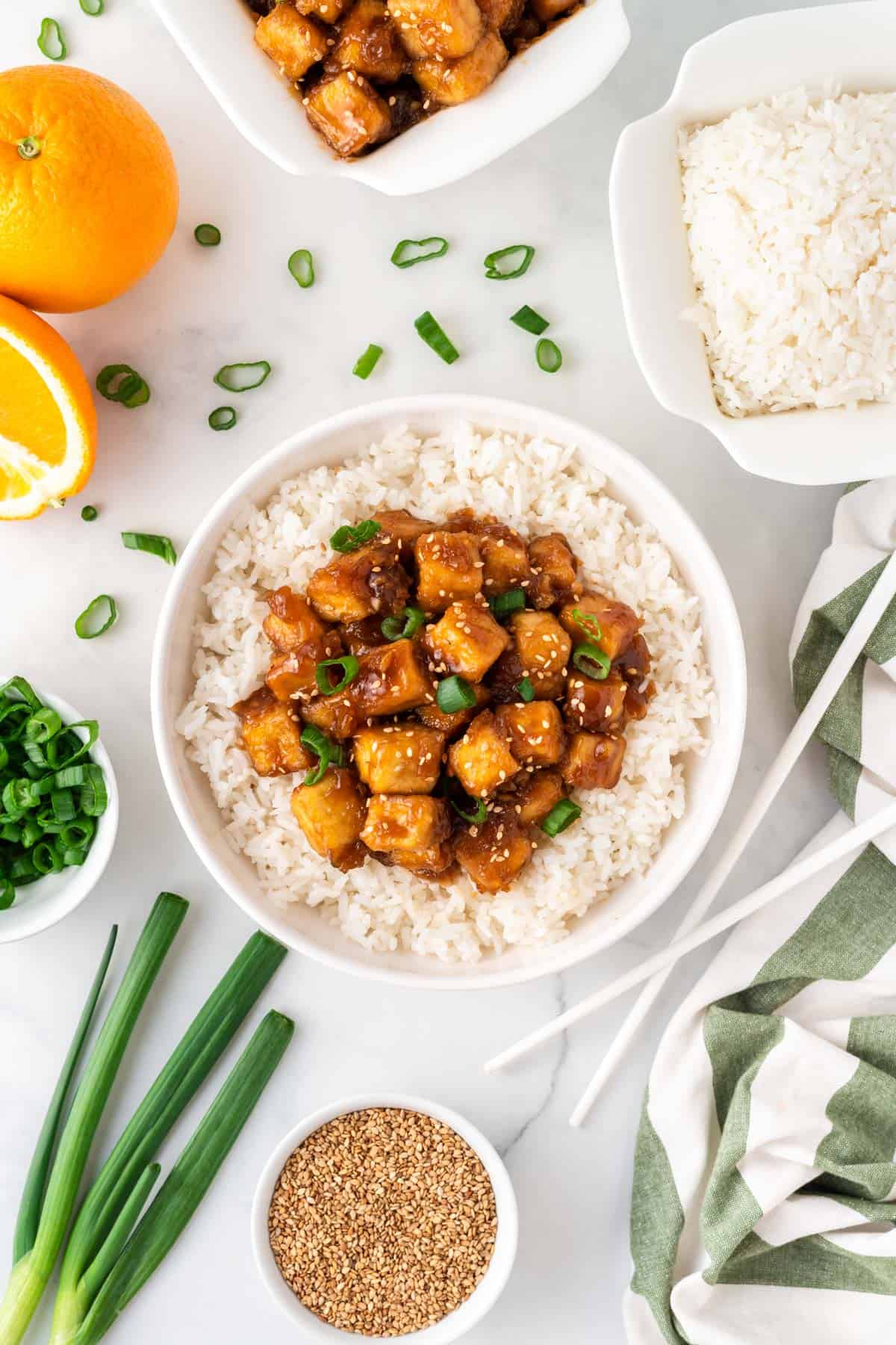 orange tofu over rice in a bowl surrounded by the recipe's ingredients