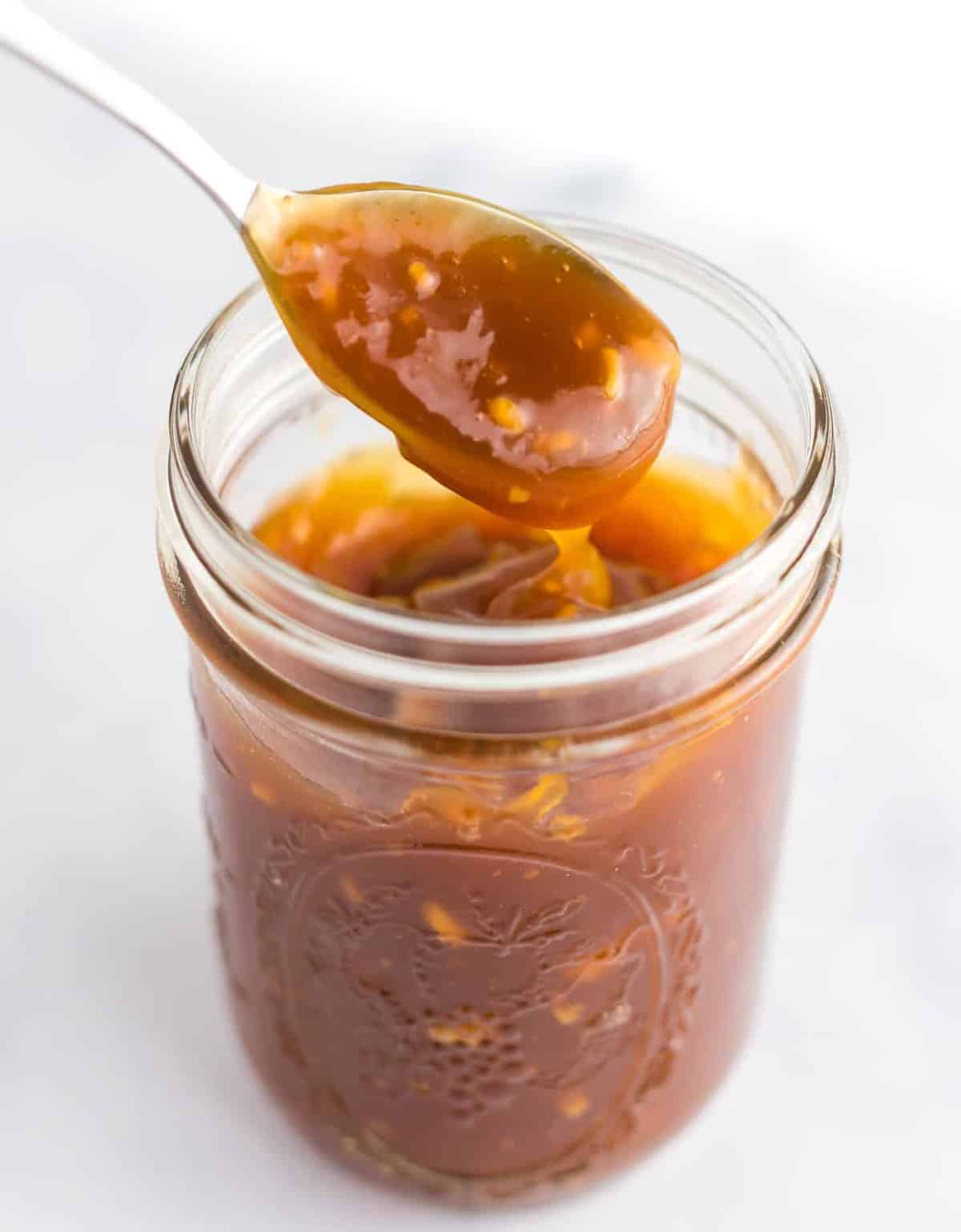 a spoon taking a dip of orange sauce for orange tofu or orange chicken