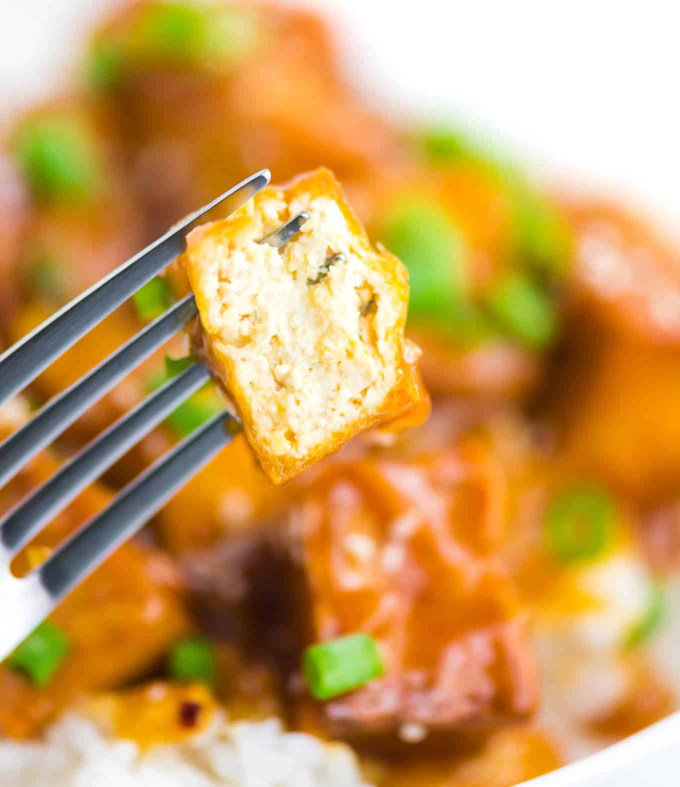 a fork with a piece of orange tofu with a bite taken out