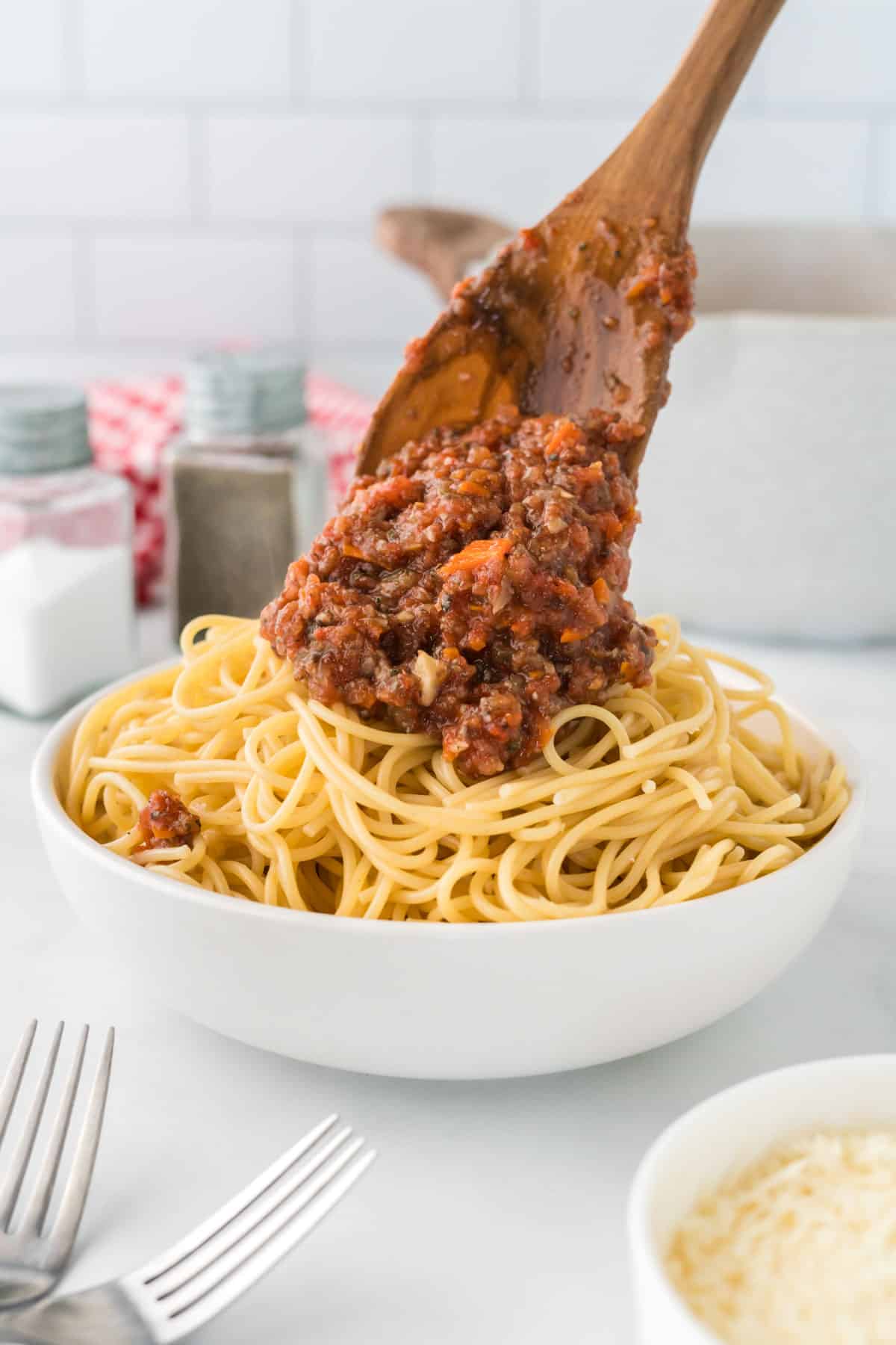 wooden spoon adding bolognese sauce to a bowl of spaghetti noodles
