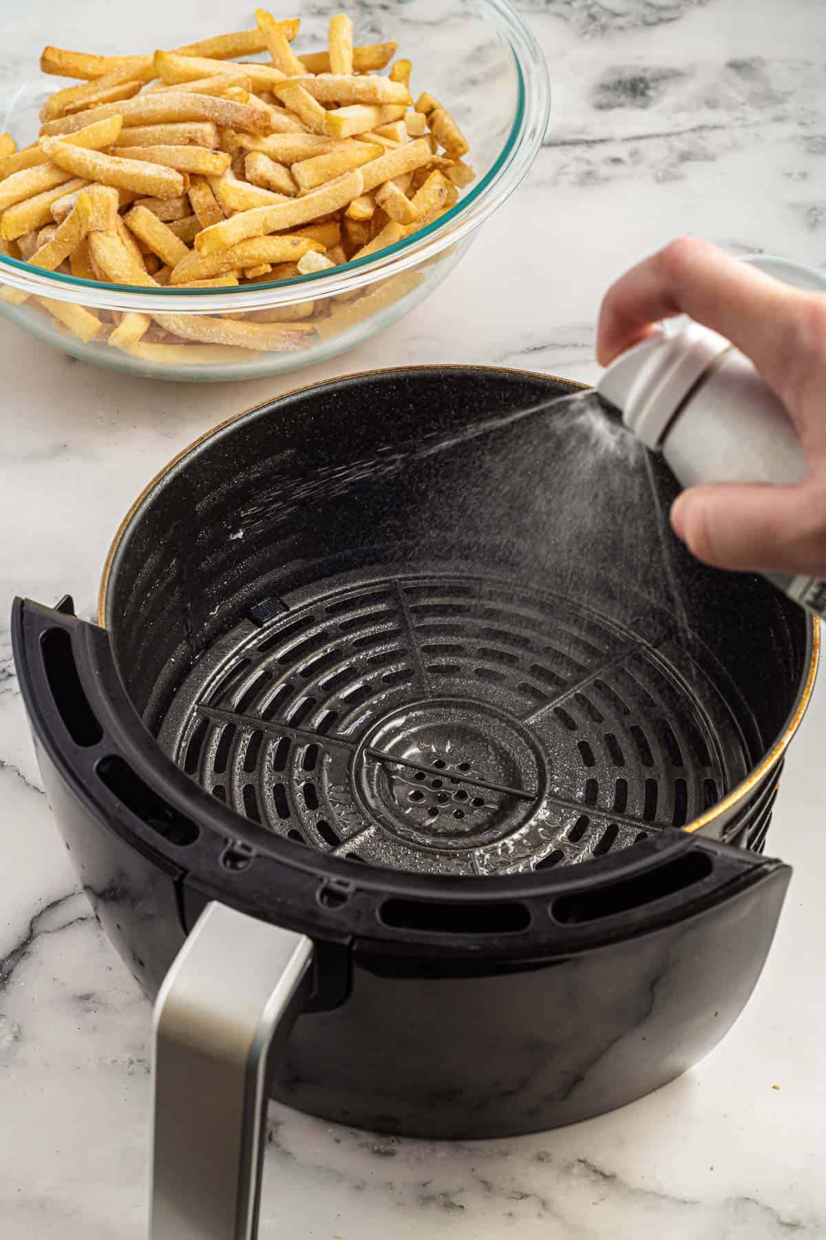 spraying oil into an air fryer basket