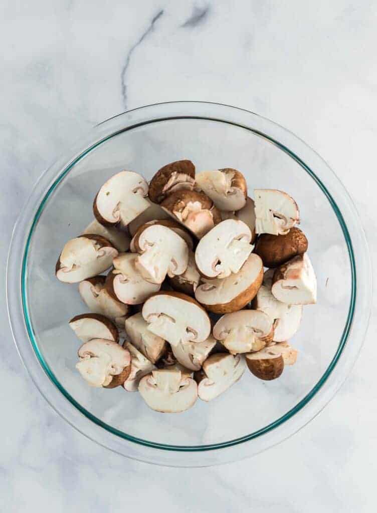 raw baby bella mushrooms cut in half in a glass bowl