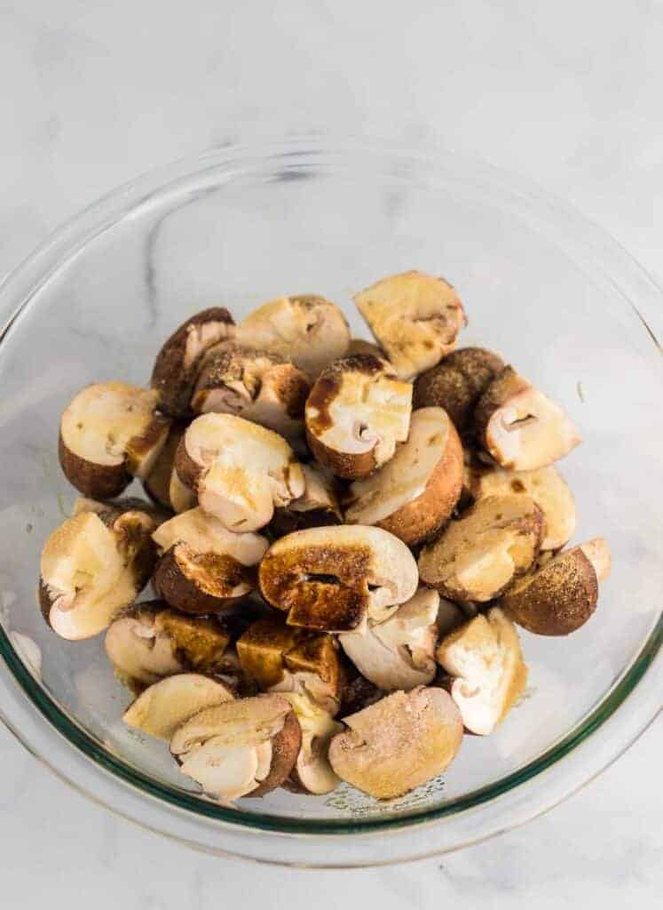 halved baby bella mushrooms in a glass bowl with spices and Worcestershire sauce