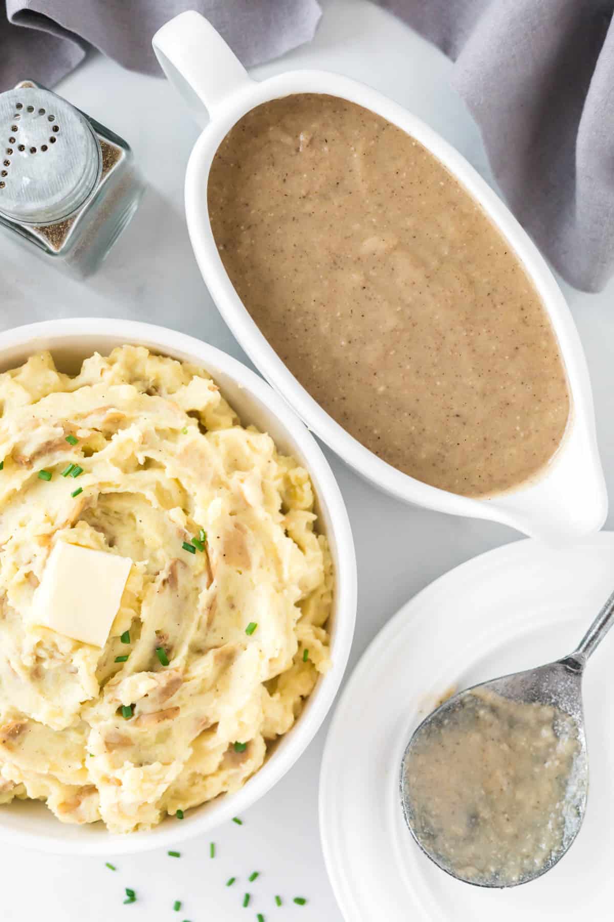 mashed potatoes in a bowl topped with butter next to a gravy boat