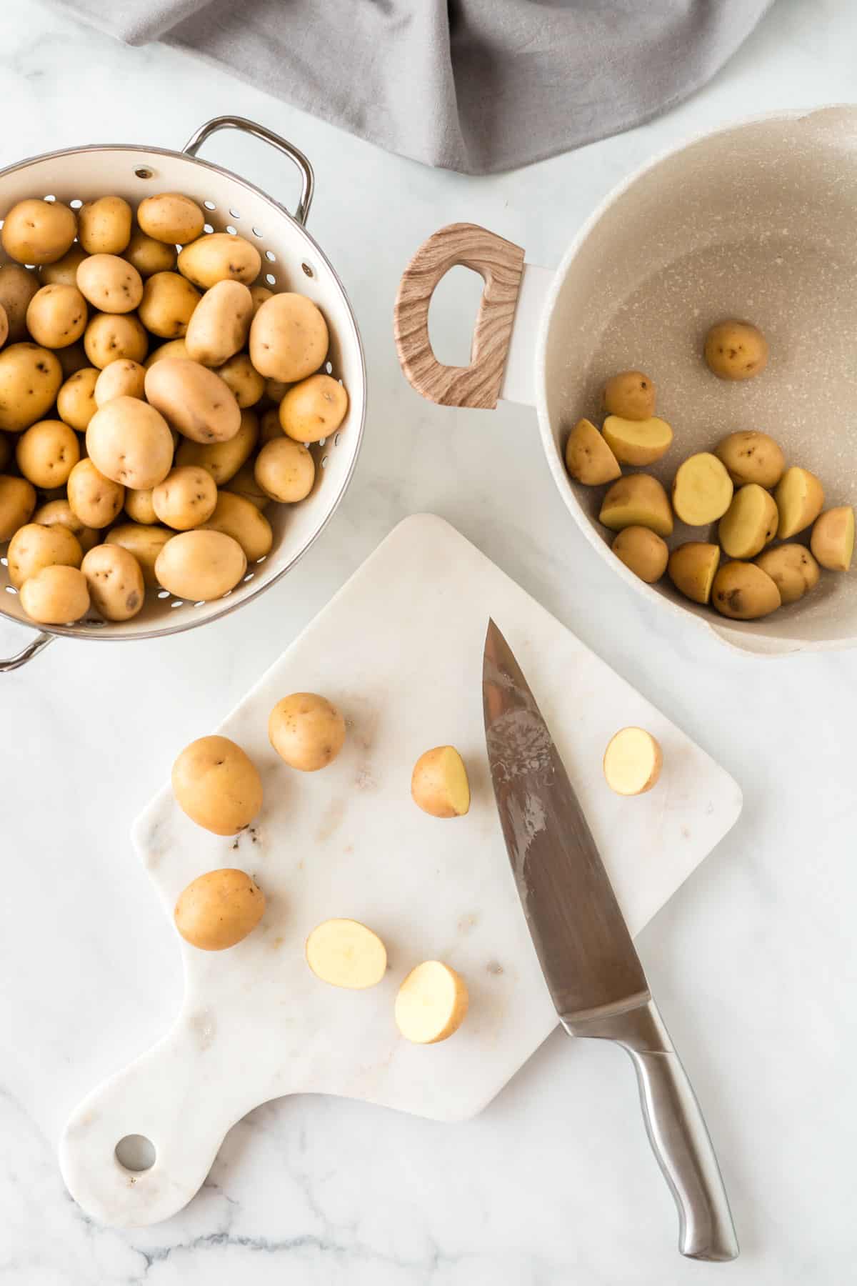 cutting board showing potatoes being cut in half and placed in a pot