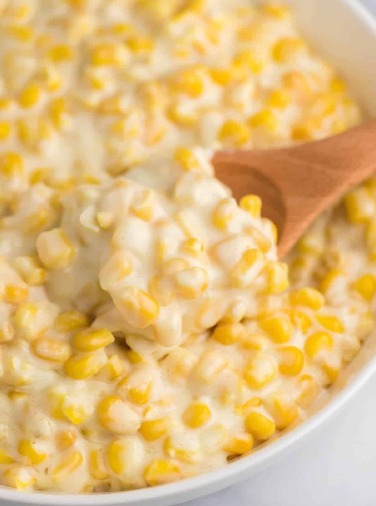 a wooden spoon taking a scoop of creamed corn