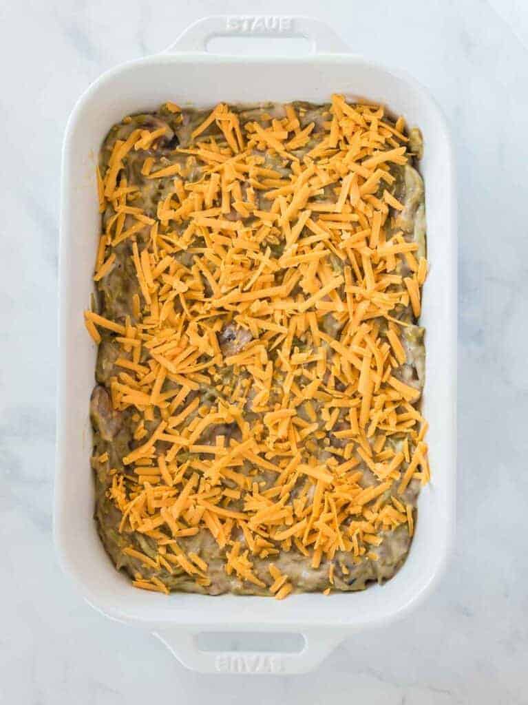 casserole filling topped with grated cheddar cheese in a white baking dish