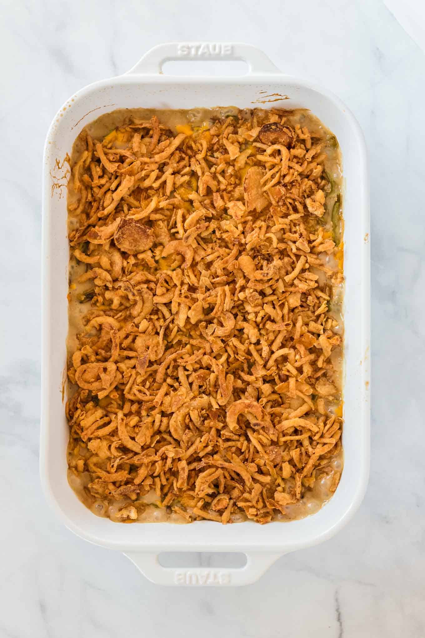 green bean casserole topped with golden french fried onions in a white baking dish