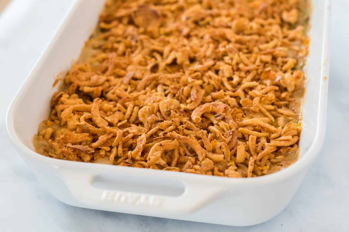 green bean casserole topped with golden french fried onions in a white baking dish
