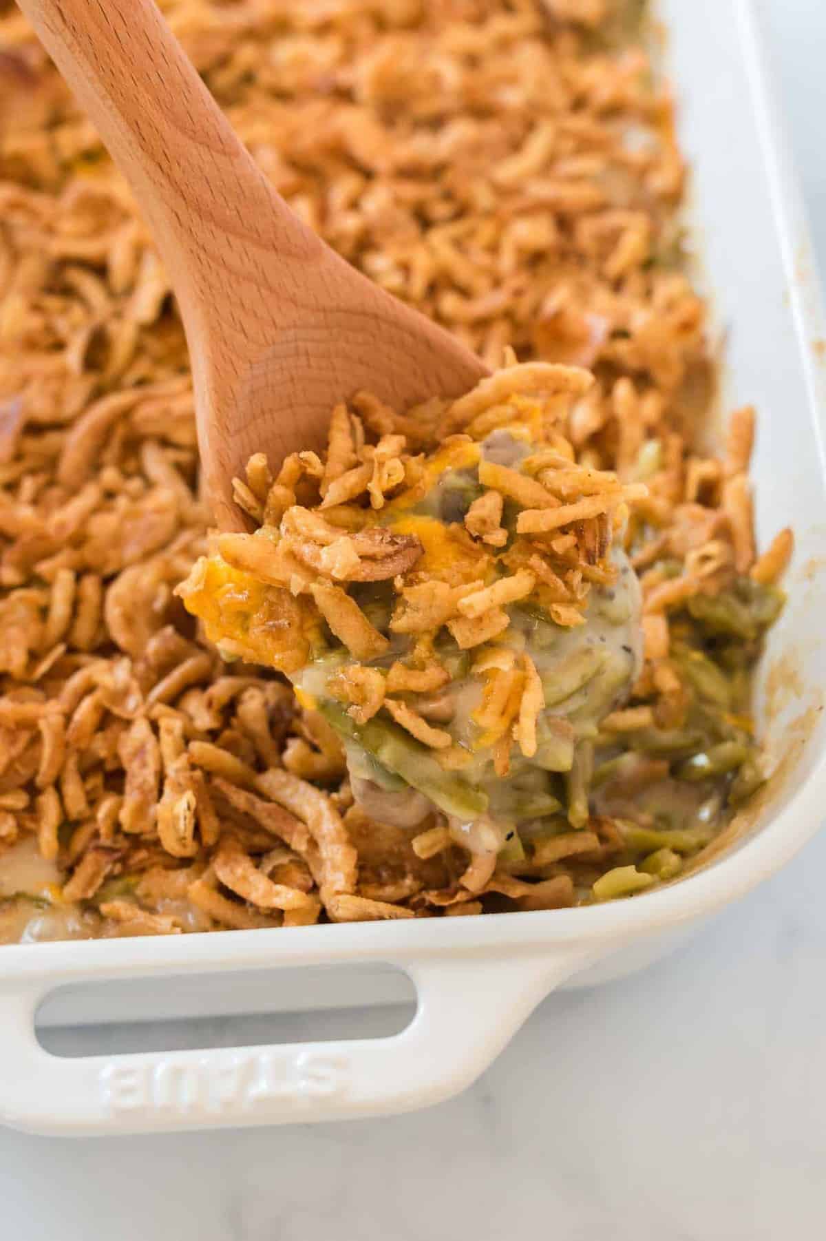 green bean casserole with a wooden spoon taking a scoop out