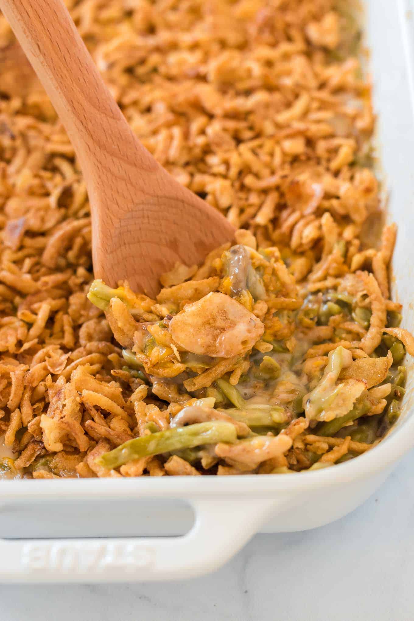 green bean casserole with a wooden spoon taking a scoop out