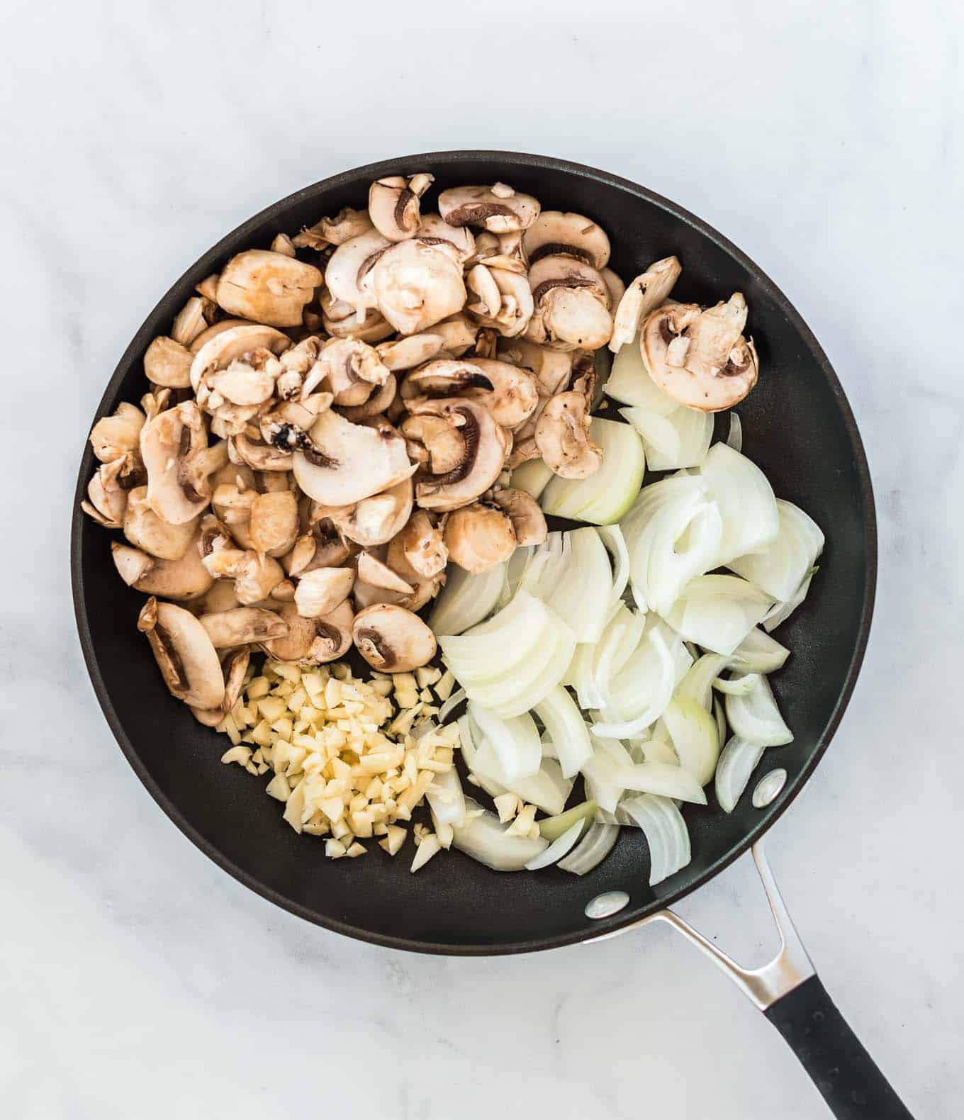 a skillet with mushrooms, minced garlic, and chopped onion in it