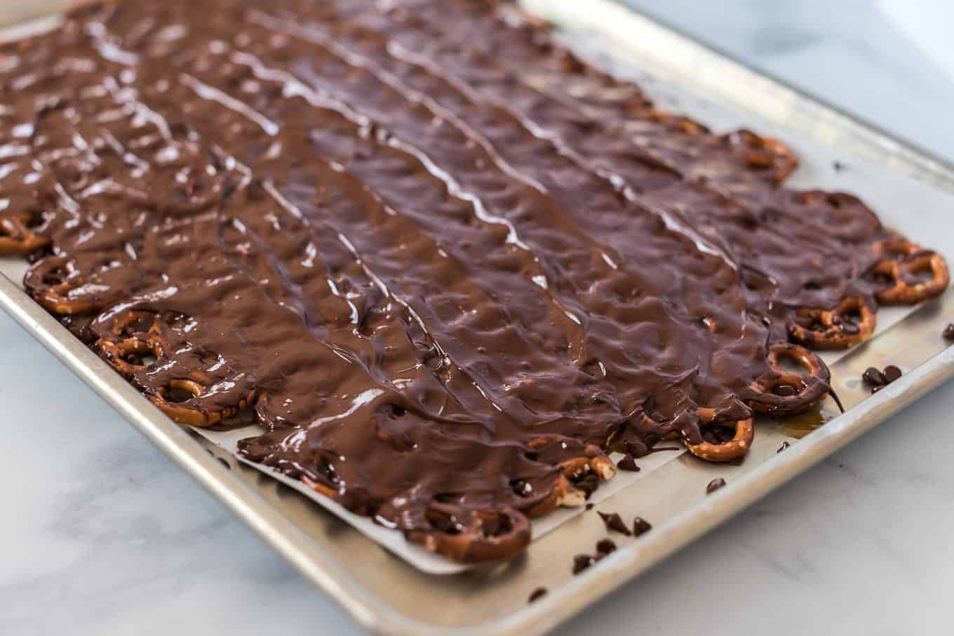 melted chocolate spread over pretzels on a baking sheet
