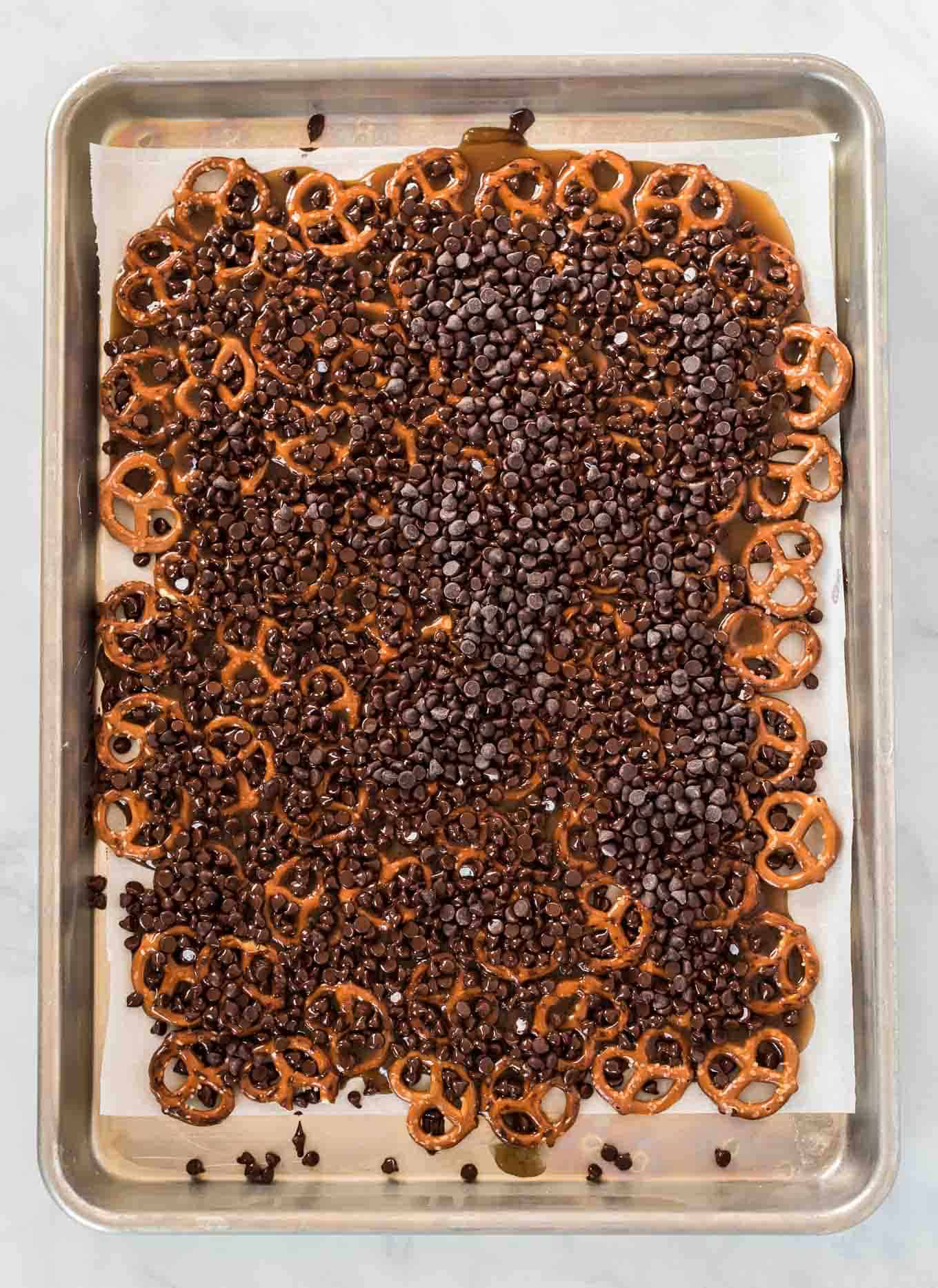 a baking sheet with pretzels covered in caramel and chocolate chips on top