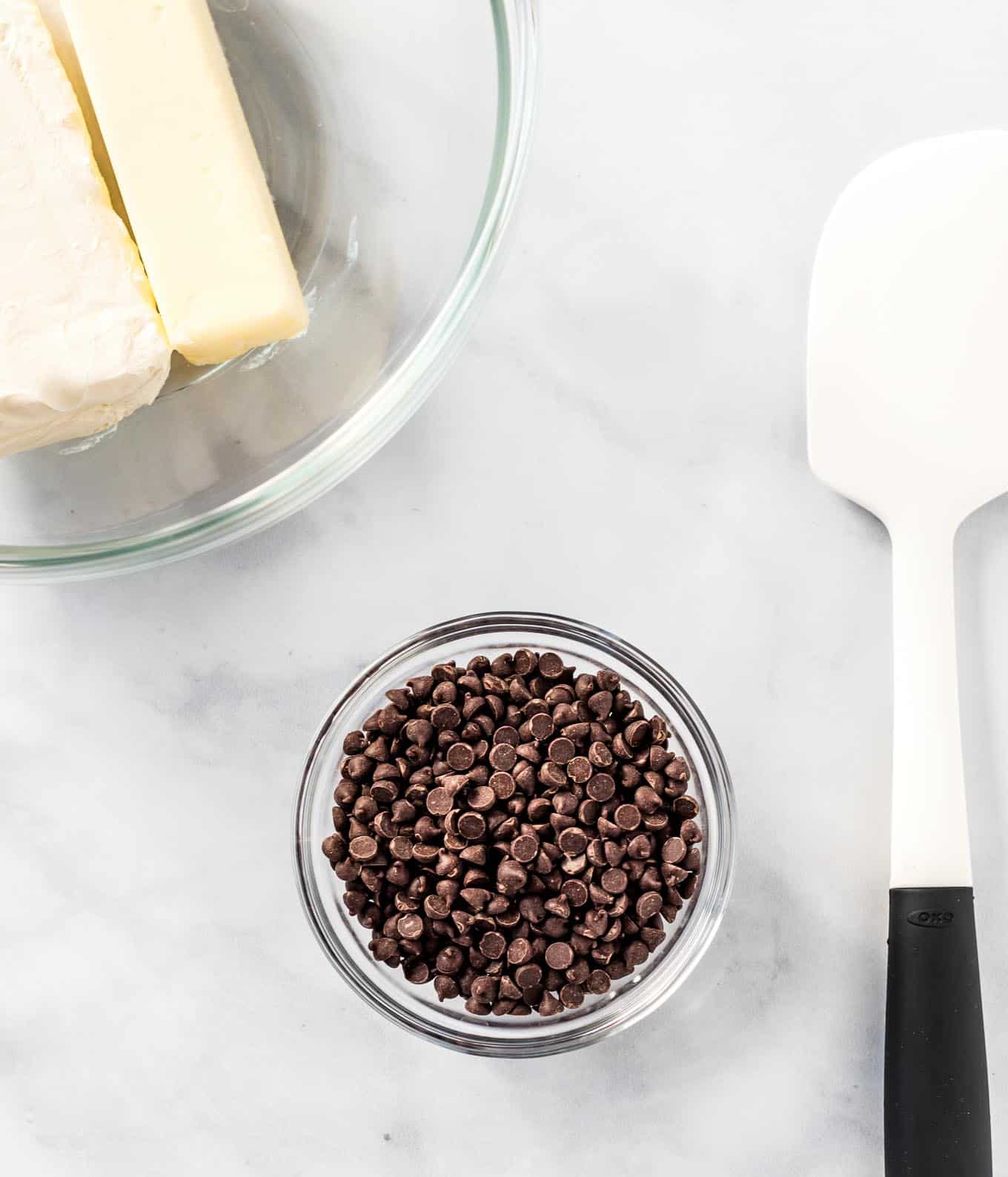 mini chocolate chips in a glass bowl with a spatula and ingredient bowl on the sides