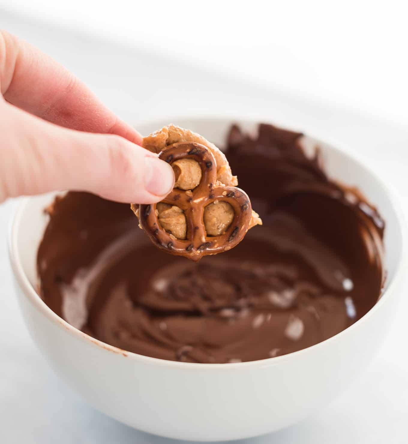 a hand holding a peanut butter stuffed pretzel over a bowl of melted chocolate