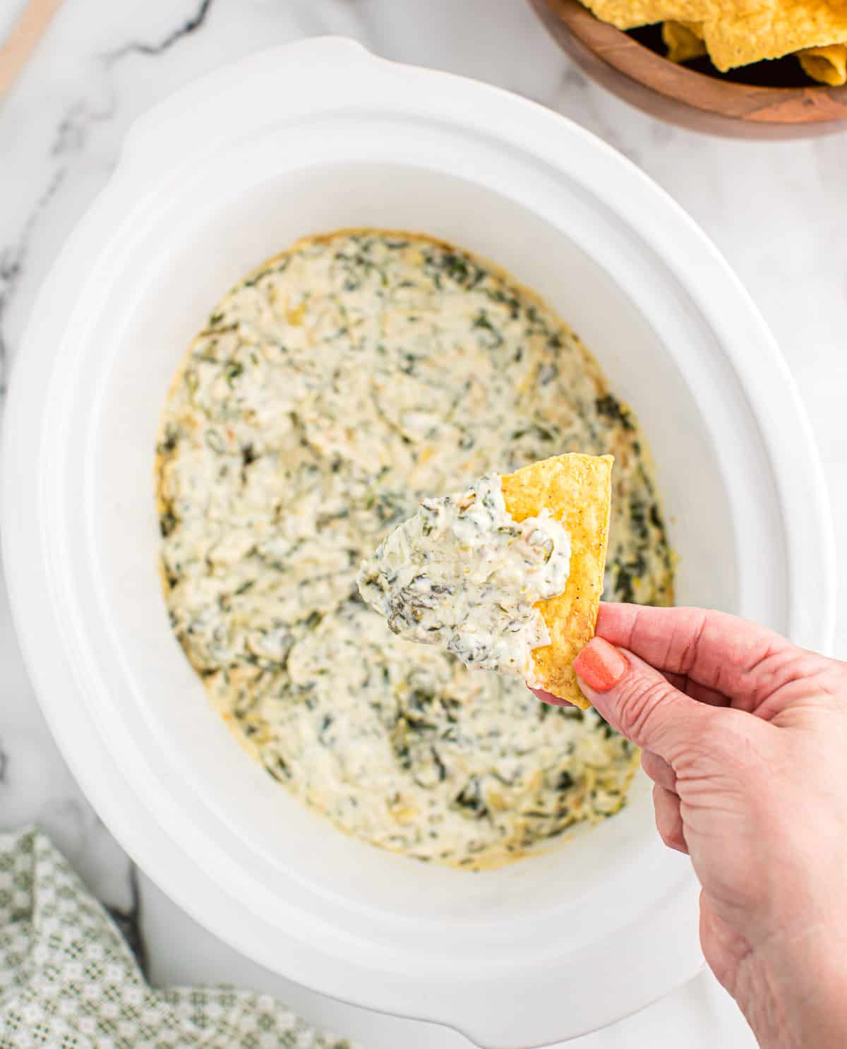 dipping a chip into a slow cooker full of spinach artichoke dip
