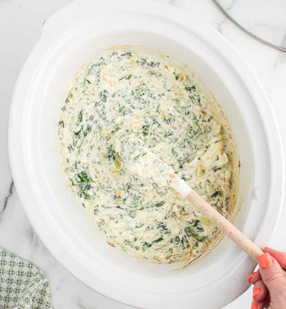 creamy slow cooker spinach artichoke dip being stirred