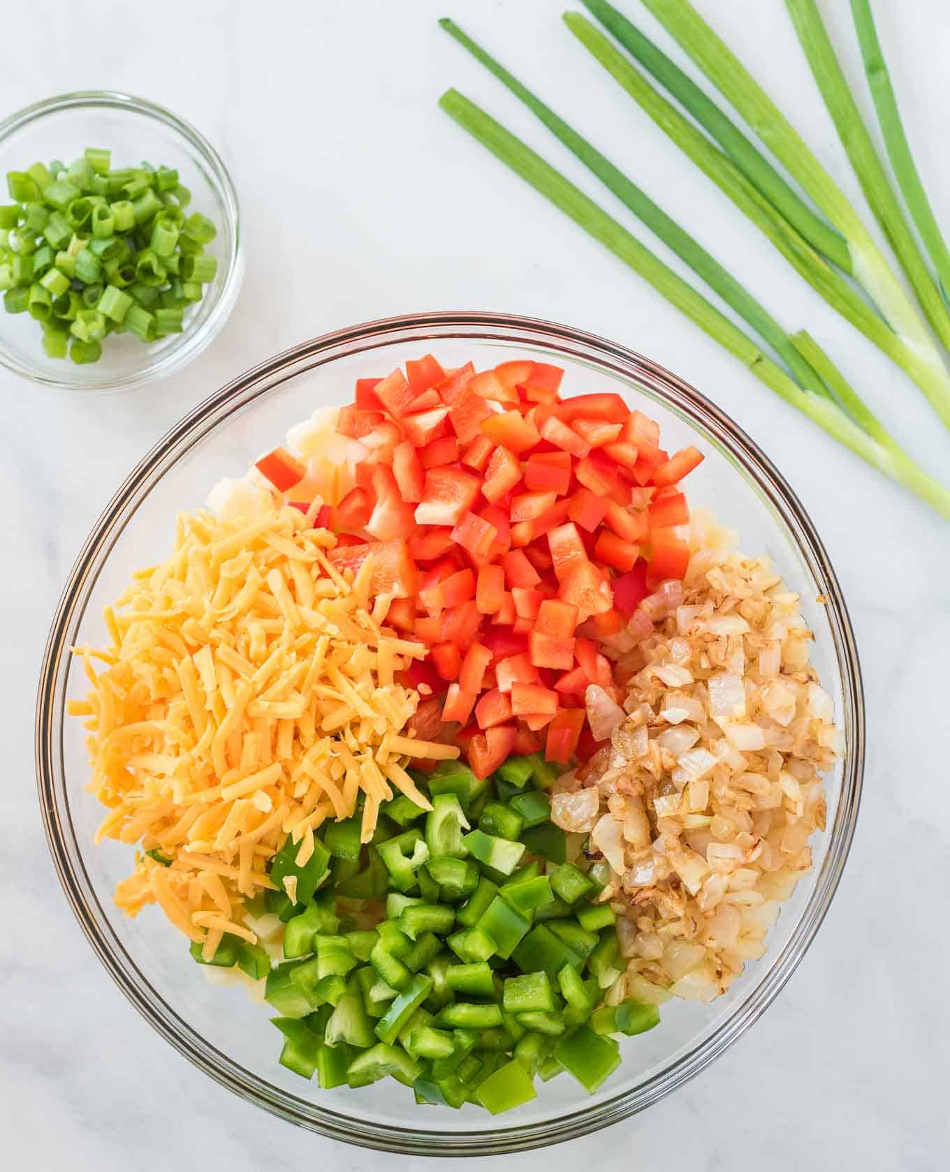 potatoes, bell pepper, onion, and cheese together in a glass mixing bowl