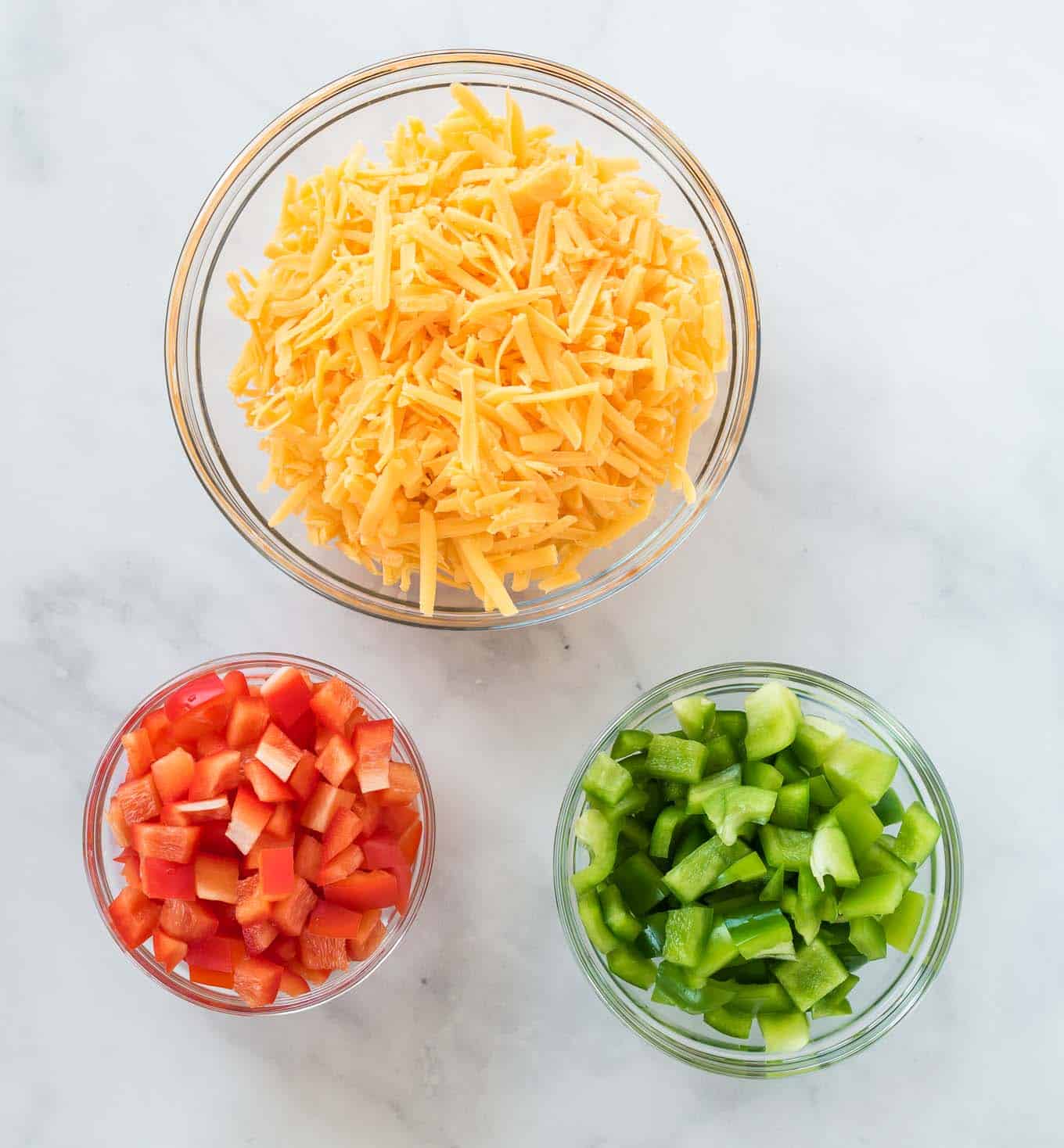 cheese, red bell pepper, and green bell pepper in separate glass bowls