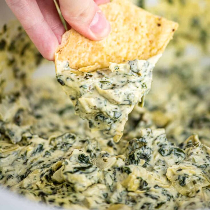 tortilla chip being dipped in spinach artichoke dip